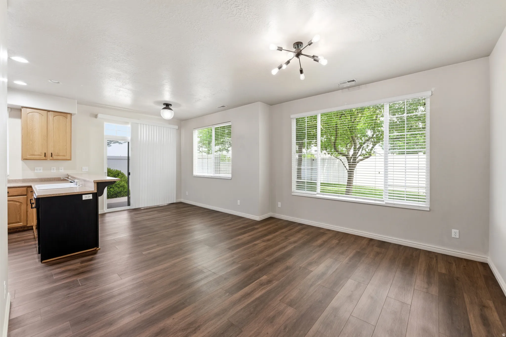Open-concept living space featuring wood-finish flooring, a contemporary ceiling light fixture, and a large window overlooking exterior greenery