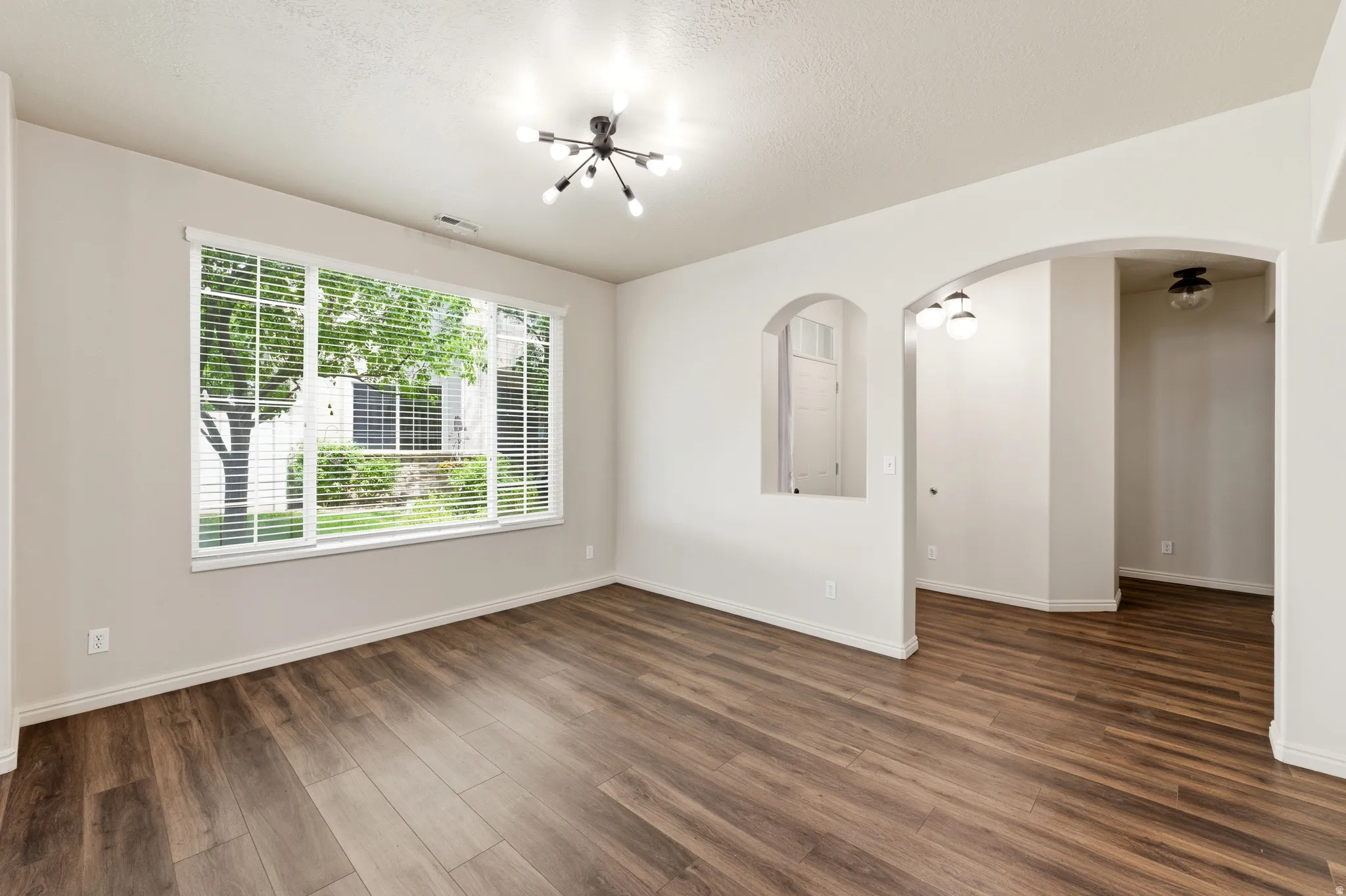 Spacious interior room featuring wood-finish flooring, a large window with horizontal blinds, and a modern ceiling light fixture