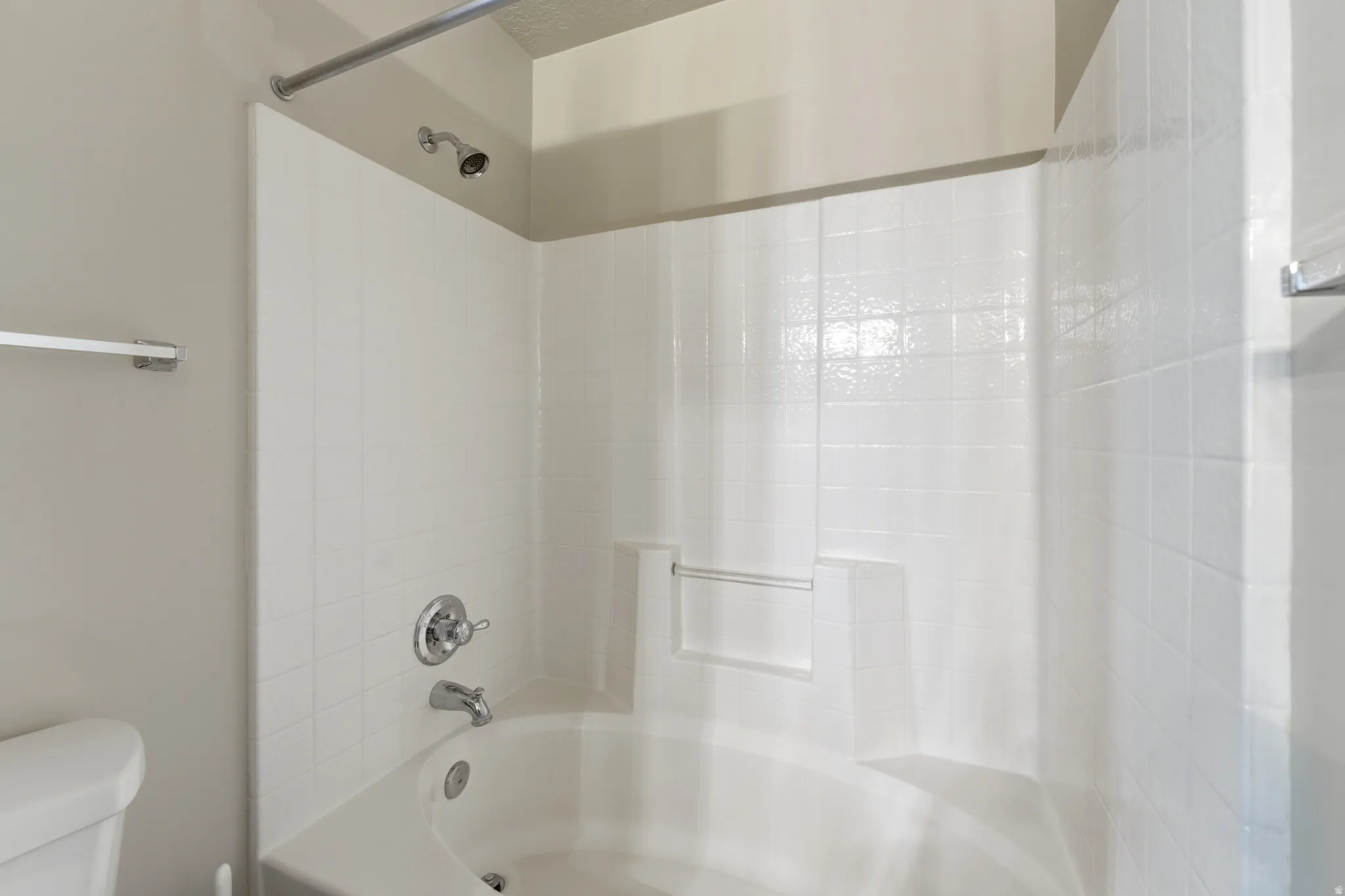 White bathtub with integrated shower, featuring a chrome shower head and faucet Primary Bath