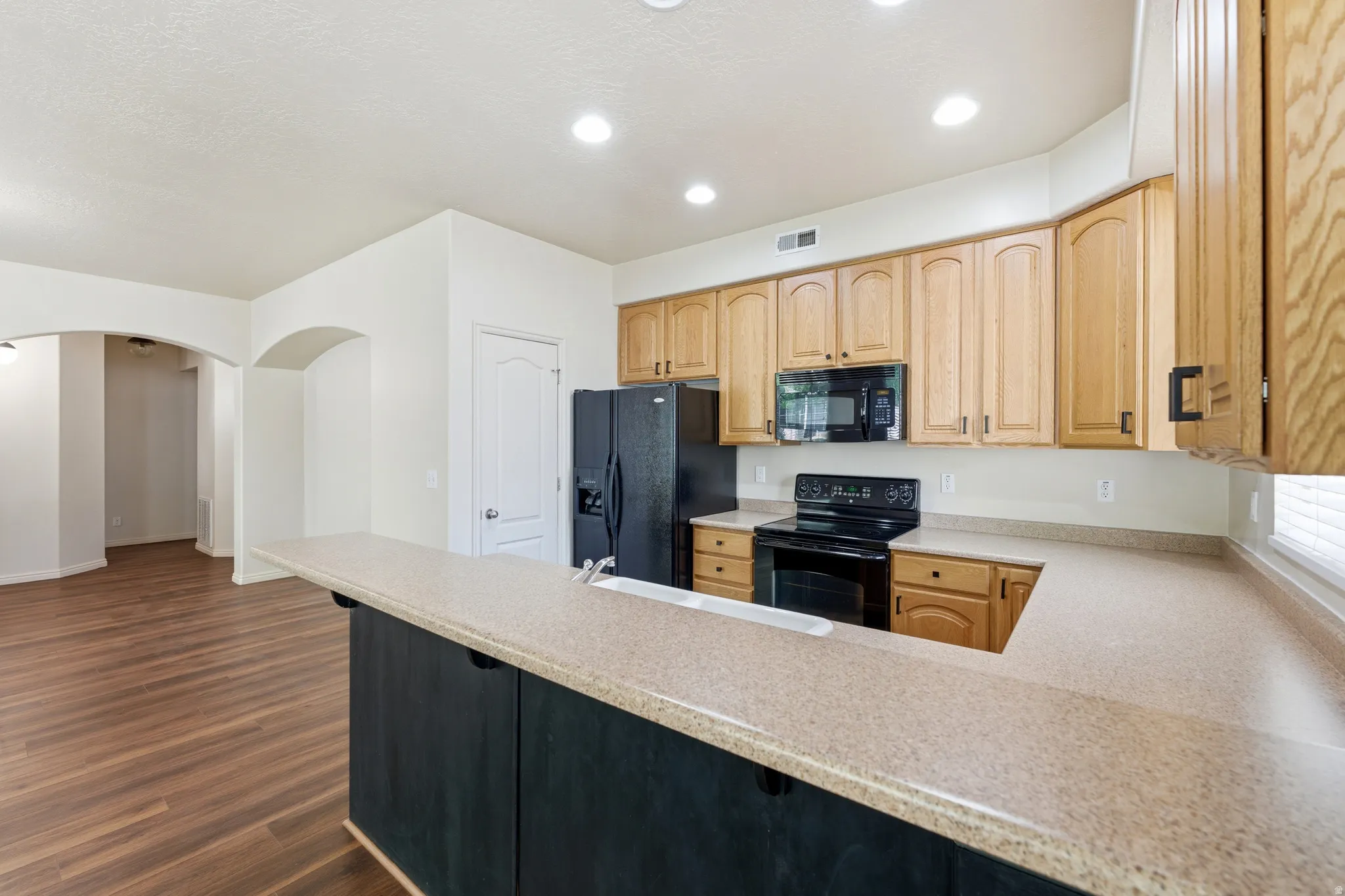 Kitchen featuring light wood cabinetry, black appliances, composite countertops, recessed lighting, and wood-finish flooring