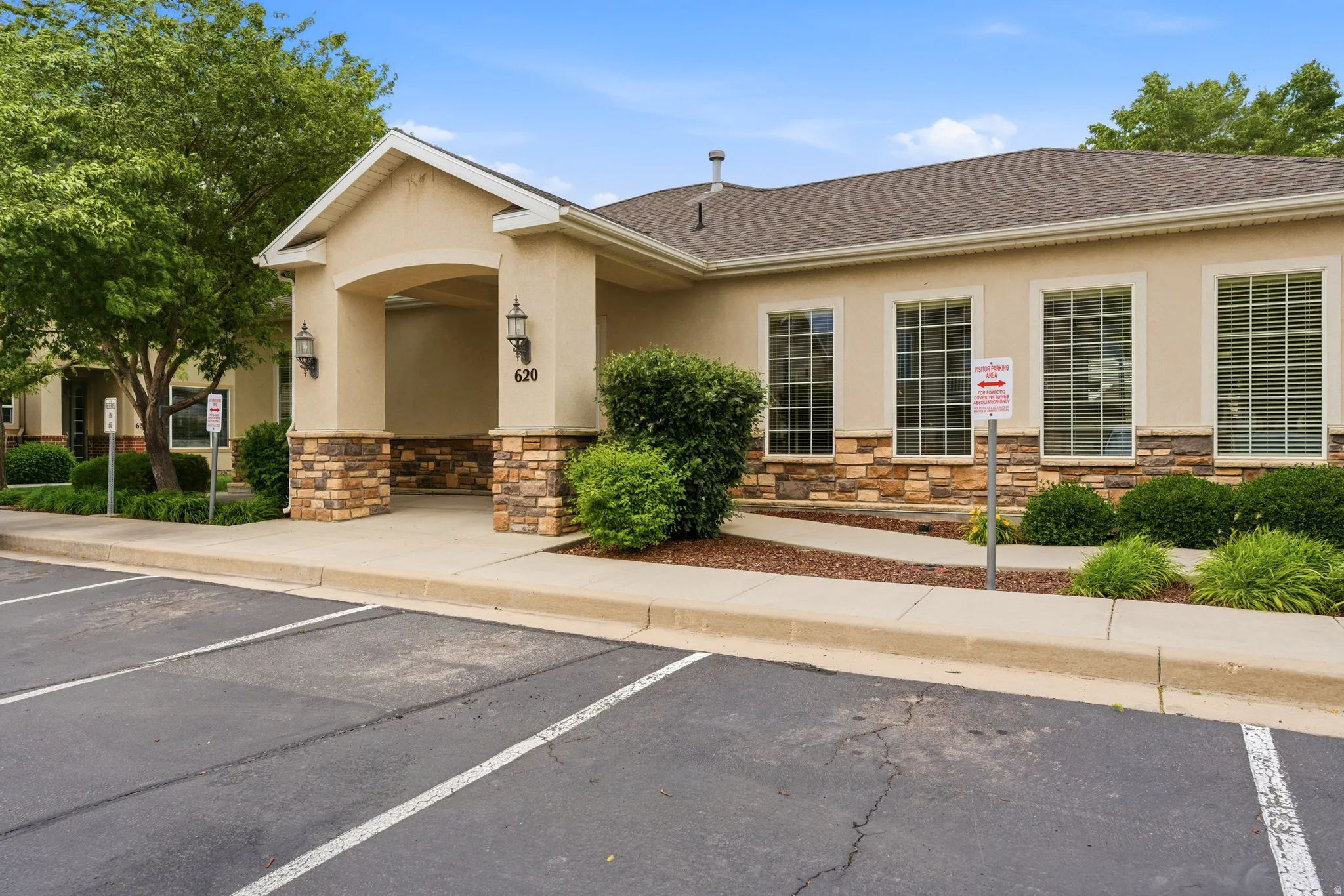 Club house Stucco exterior featuring stone accents, multiple large windows with grid patterns, and a covered entry with exterior sconces