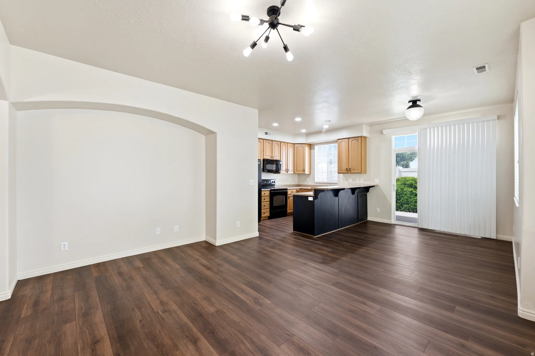 Spacious living area featuring wood-finish flooring, an arched entryway, and a modern chandelier