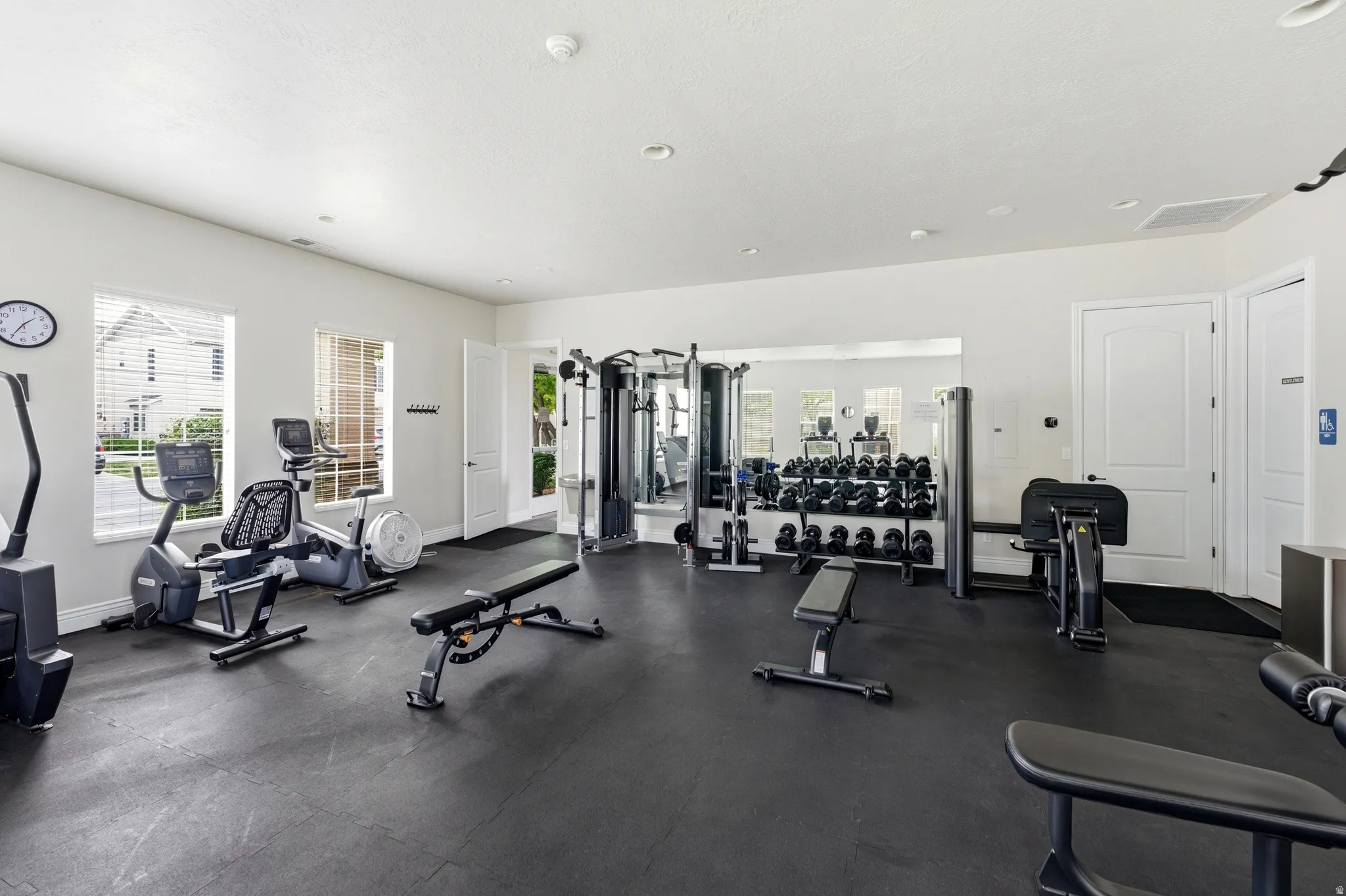 In club House Dedicated fitness room featuring rubber flooring, abundant natural light from multiple windows, and a mirrored wall