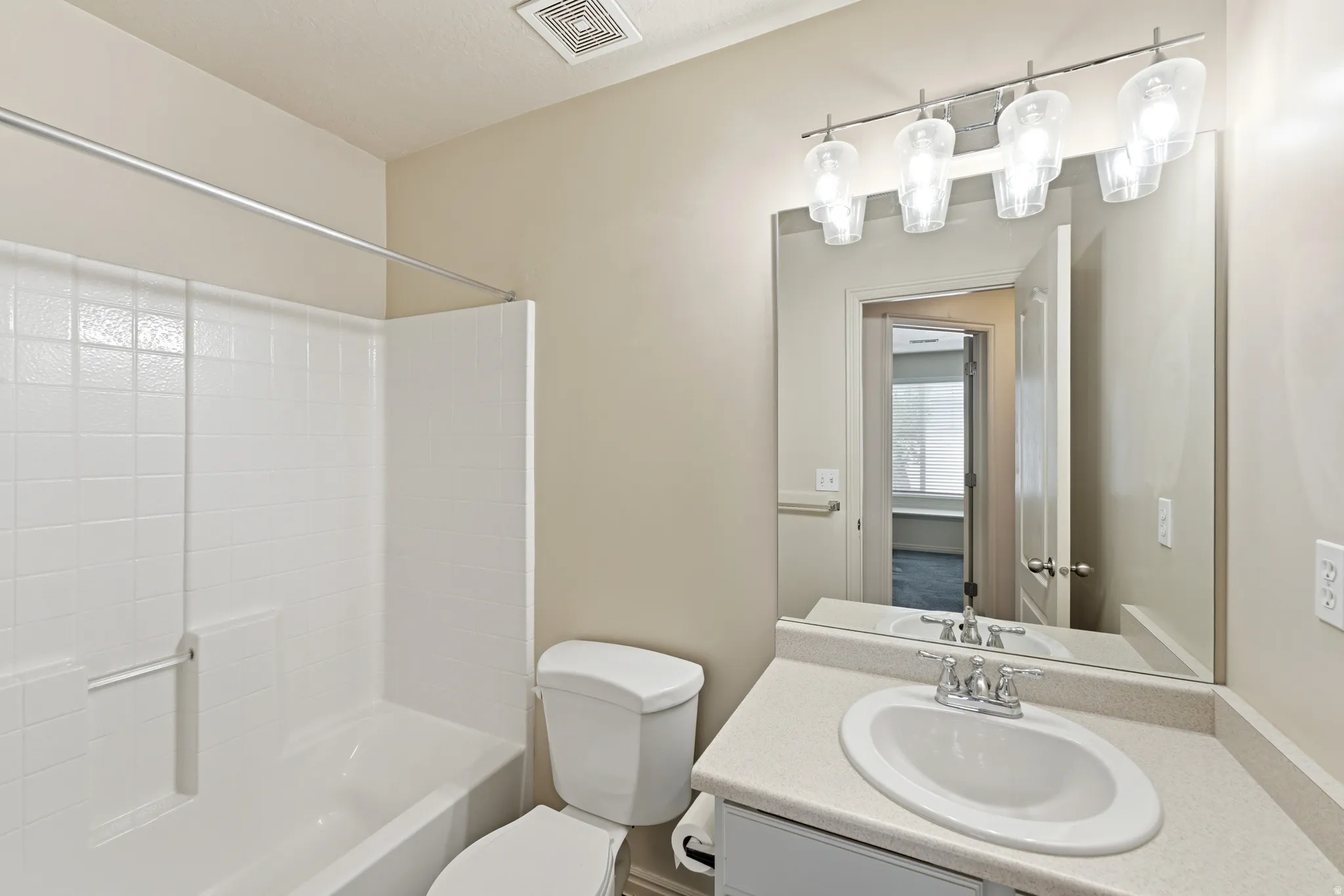 Guest Bathroom featuring a built-in tub with white tile surround, a single vanity with an integrated sink, a large mirror, and a four-light fixture