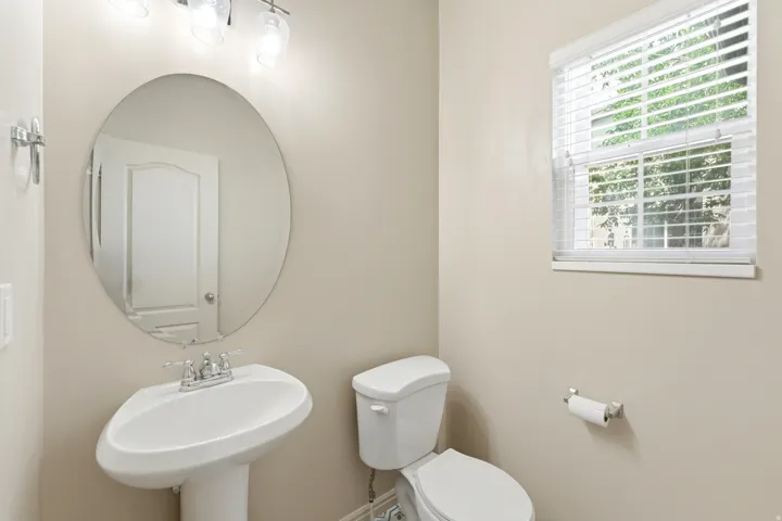 Pedestal sink with chrome faucet, oval mirror, and three-light vanity fixture