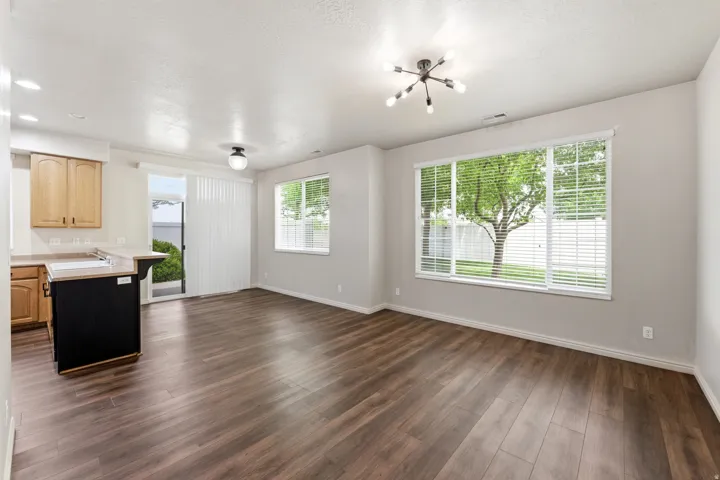 Open-concept living space featuring wood-finish flooring, a contemporary ceiling light fixture, and a large window overlooking exterior greenery
