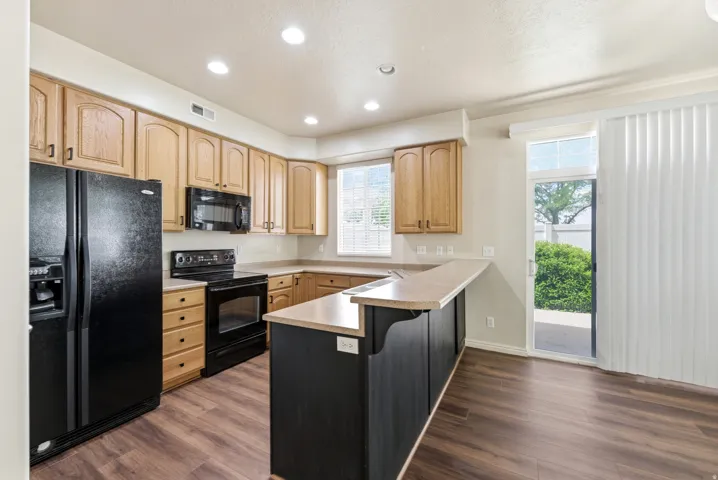 Kitchen featuring wood cabinetry, black appliances, a breakfast bar, recessed lighting, and wood-finish flooring