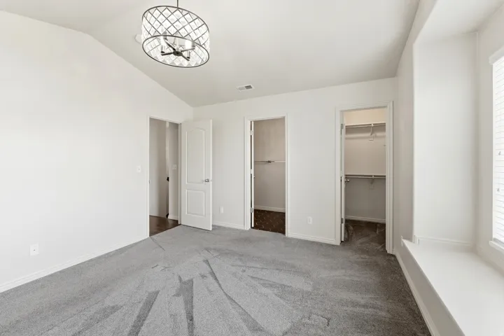 Spacious Primary bedroom featuring vaulted ceilings, a contemporary ceiling light fixture, grey carpeting, multiple door entries, and a window seat with blinds