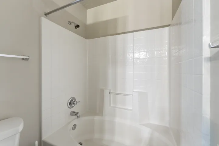 White bathtub with integrated shower, featuring a chrome shower head and faucet Primary Bath