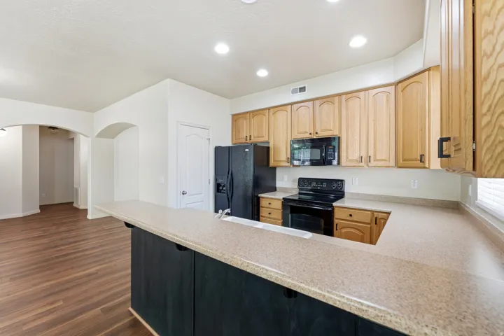 Kitchen featuring light wood cabinetry, black appliances, composite countertops, recessed lighting, and wood-finish flooring