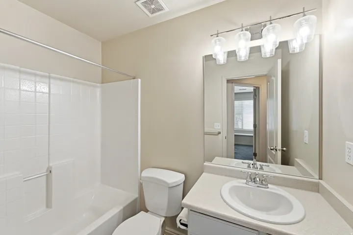 Guest Bathroom featuring a built-in tub with white tile surround, a single vanity with an integrated sink, a large mirror, and a four-light fixture
