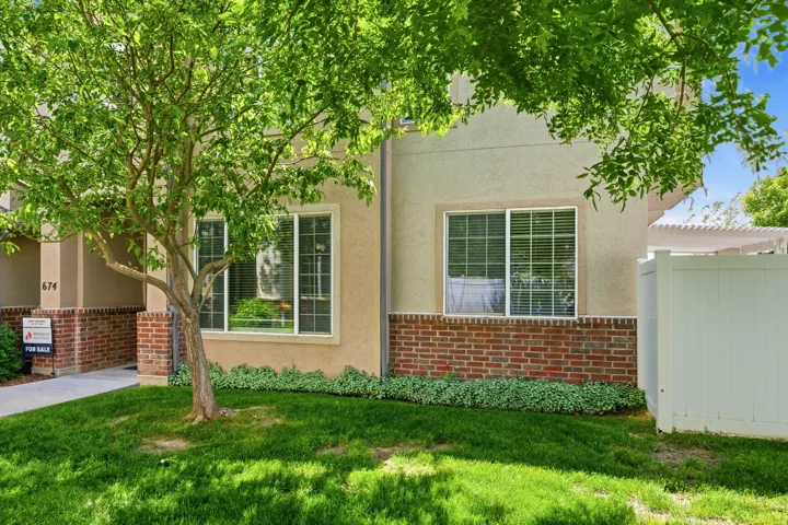 Stucco exterior featuring red brick detailing, white-trimmed windows, and a manicured lawn