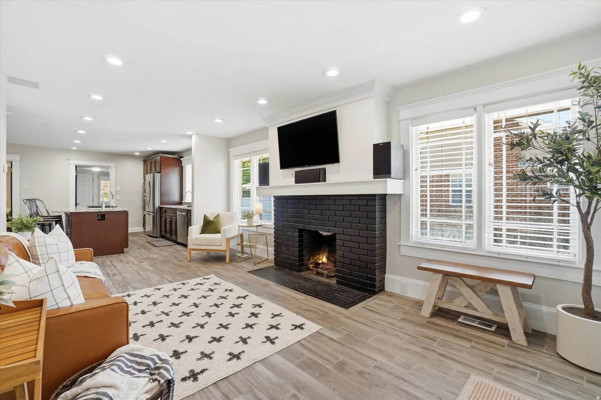 Spacious living area featuring light wood-finish flooring, recessed lighting, and a black brick fireplace with a white mantel