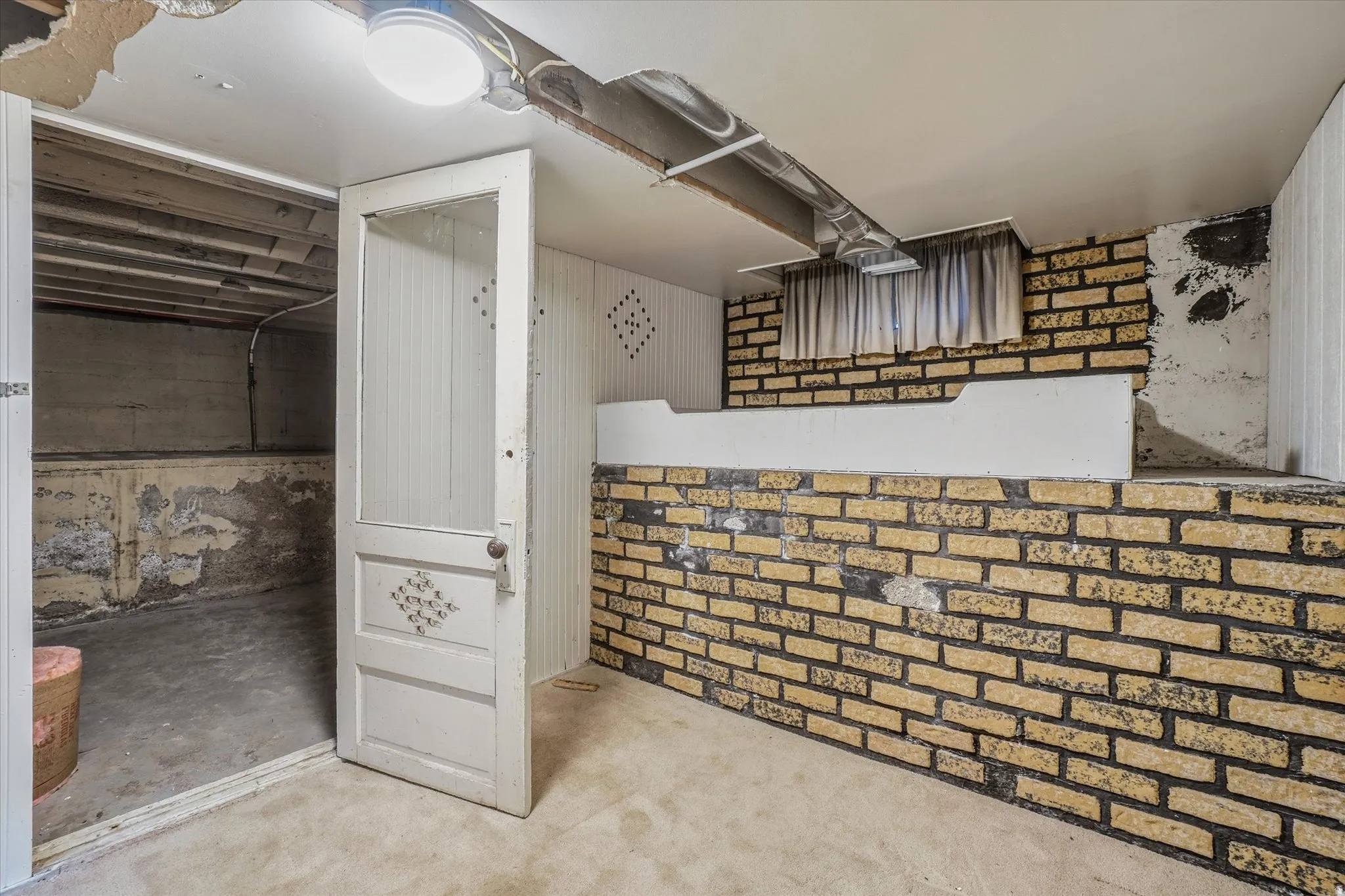 Basement space featuring exposed brickwork, beadboard paneling, and an interior door with decorative glass inserts