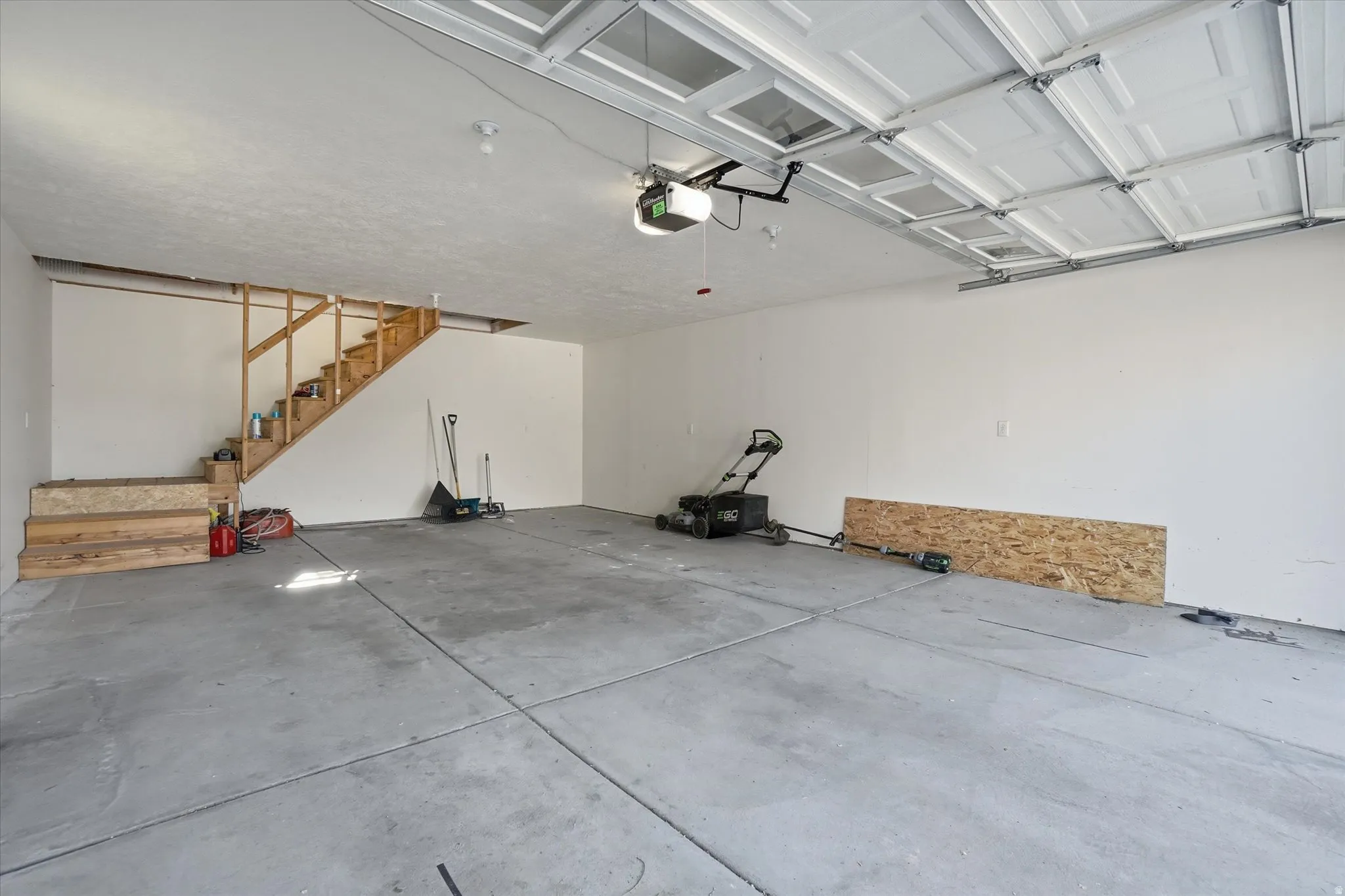 Spacious garage featuring a concrete floor, white interior walls, and an exposed wood staircase leading to an upper level
