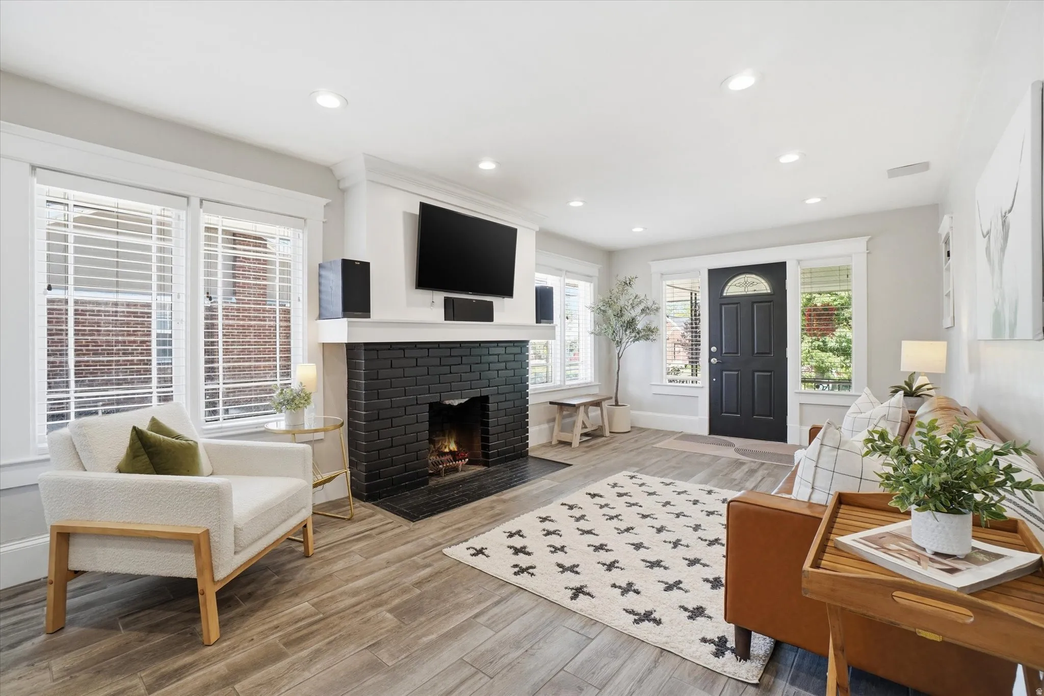 Living area featuring a black brick fireplace, wood-finish flooring, recessed lighting, and a dark-paneled entry door with an arched glass insert