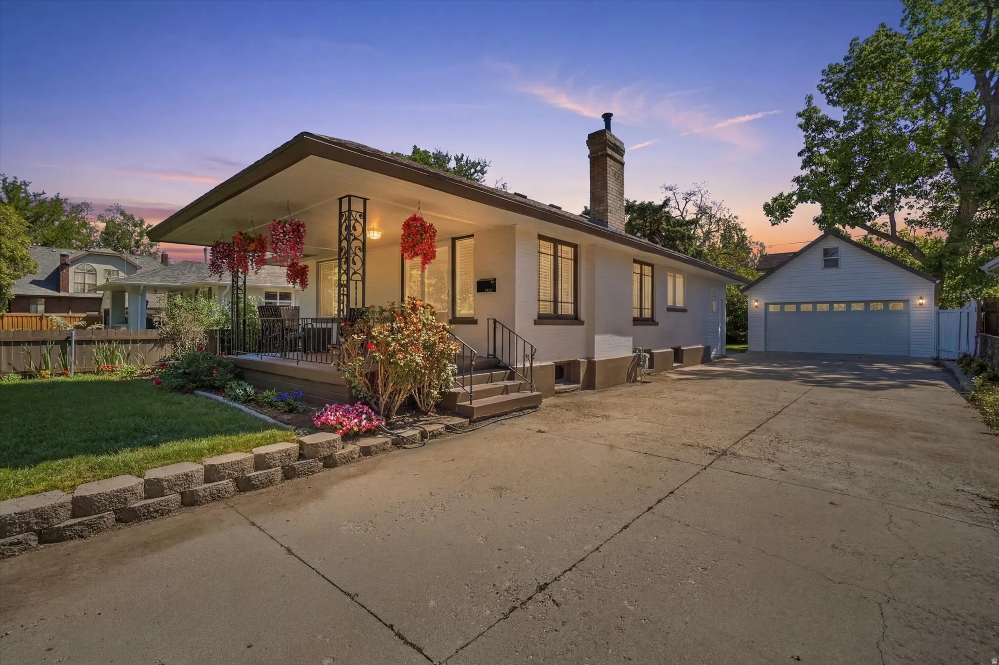Front exterior featuring a covered porch with decorative railing, manicured lawn, and a block retaining wall