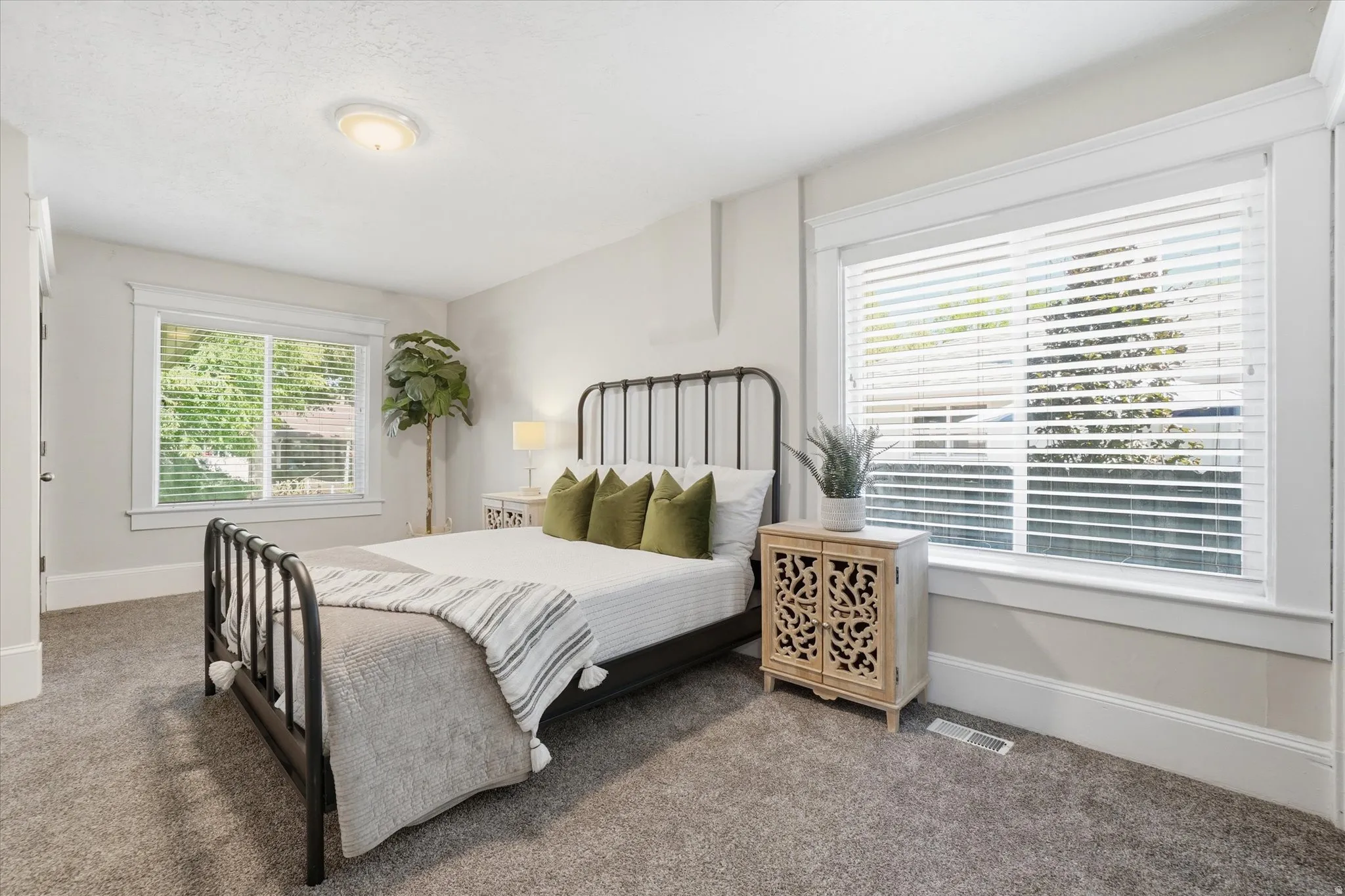 Bedroom featuring soft gray carpeting, two large windows with white blinds and trim, and a flush-mount ceiling light