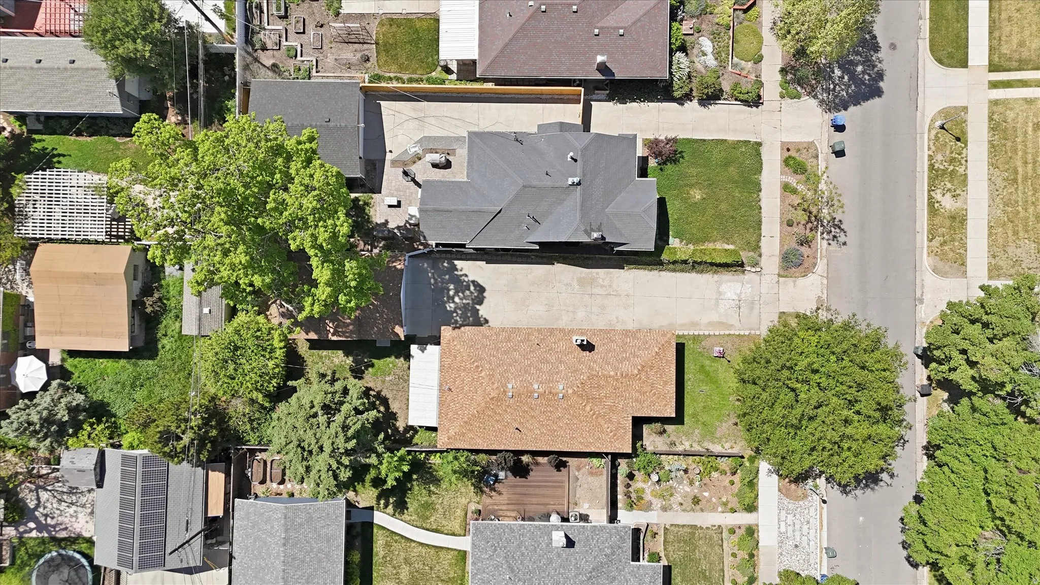 Aerial overview showcasing a property with a gray shingle roof, established landscaping, and a paved driveway