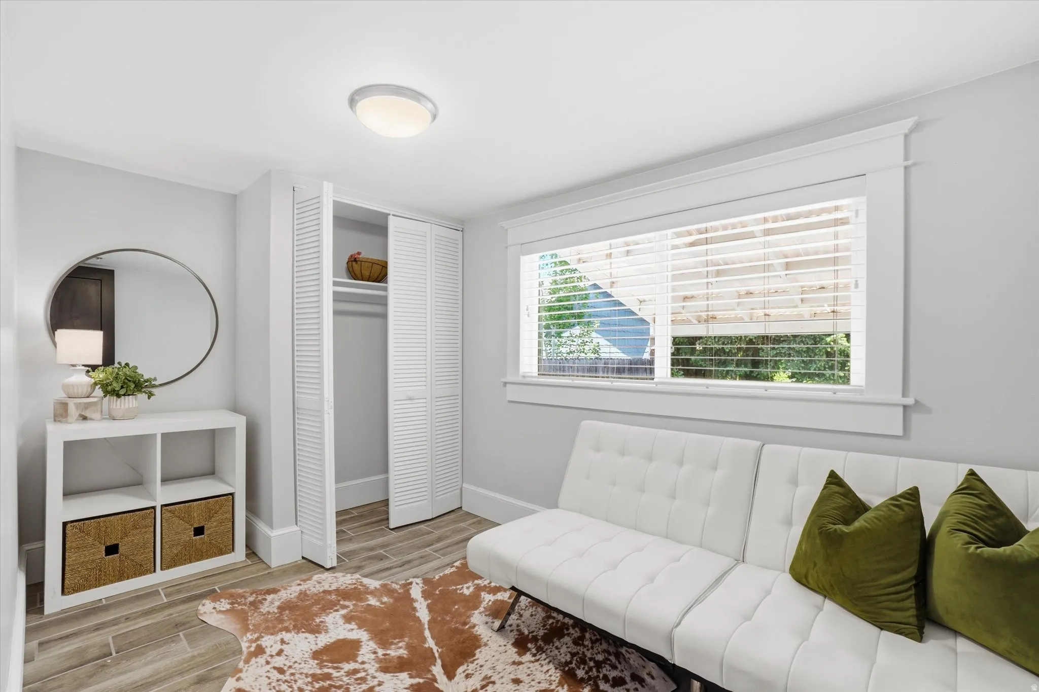 Room featuring wood-finish flooring, a bright window with white blinds, a spacious closet with louvered bifold doors, a flush-mount ceiling light, and light gray wall paint