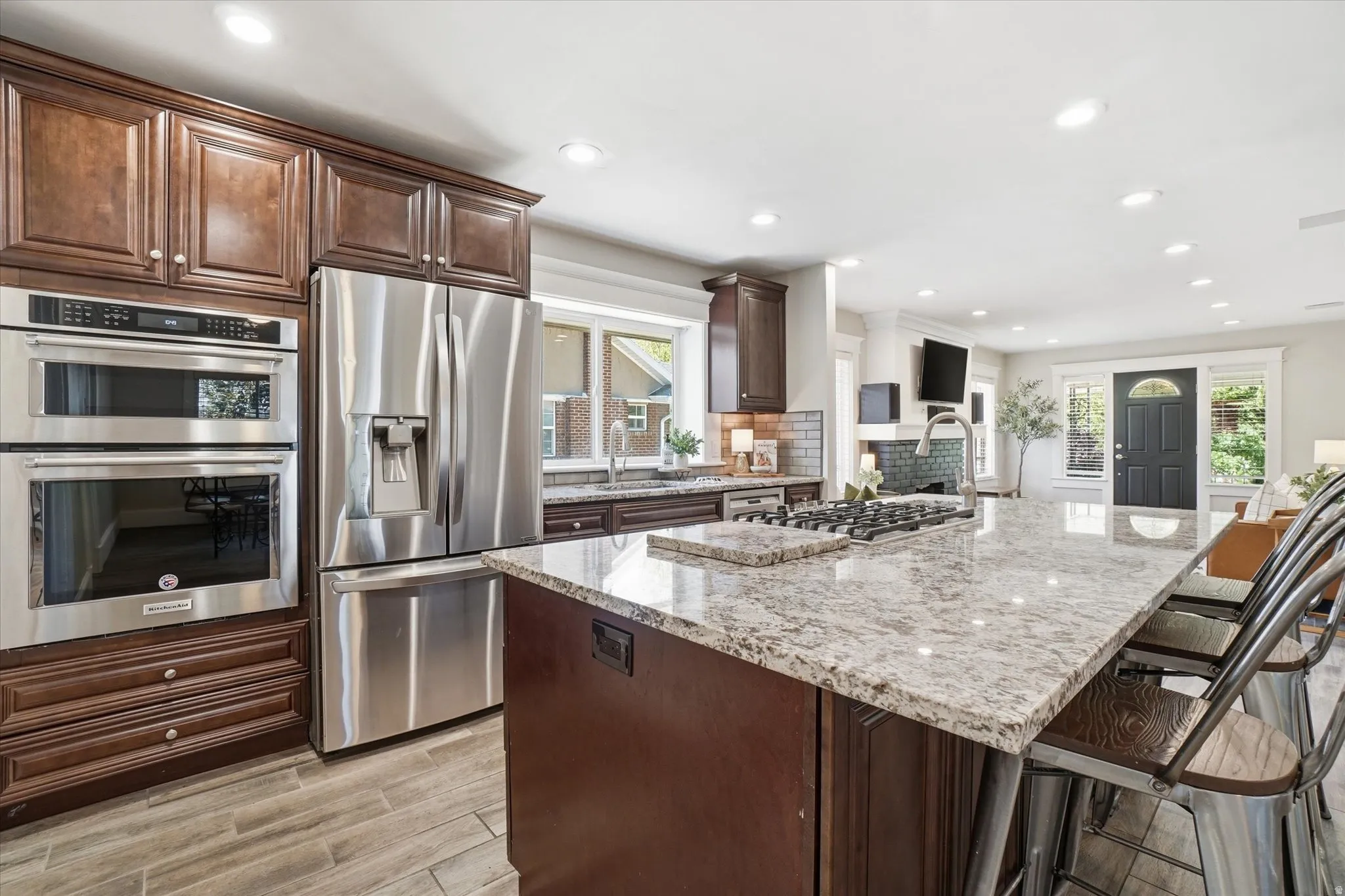 Spacious kitchen featuring an expansive island with a gas cooktop, stainless steel appliances, rich wood cabinetry, light-toned countertops, and wood-look flooring