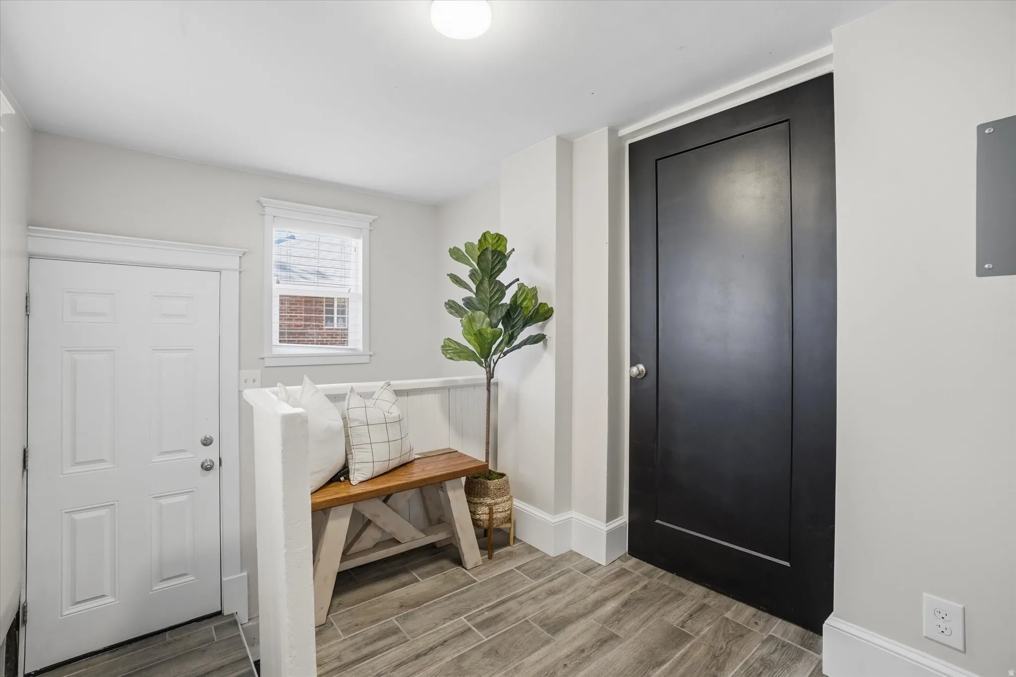 Entryway featuring wood-finish tile flooring, a white paneled door, and a contrasting black interior door