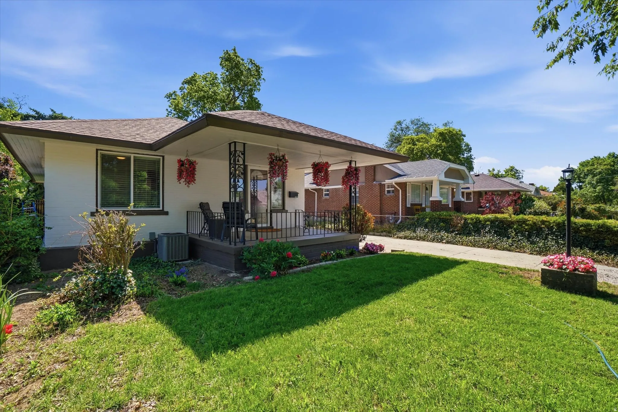 Charming single-story residence featuring a covered front porch with decorative wrought iron railings, a manicured front lawn, and a paved driveway