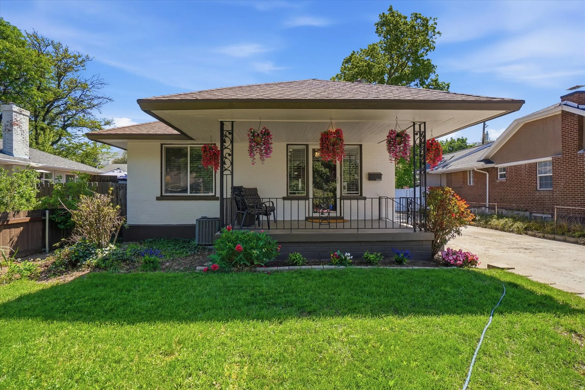 White exterior with a covered front porch featuring decorative ironwork and a manicured lawn