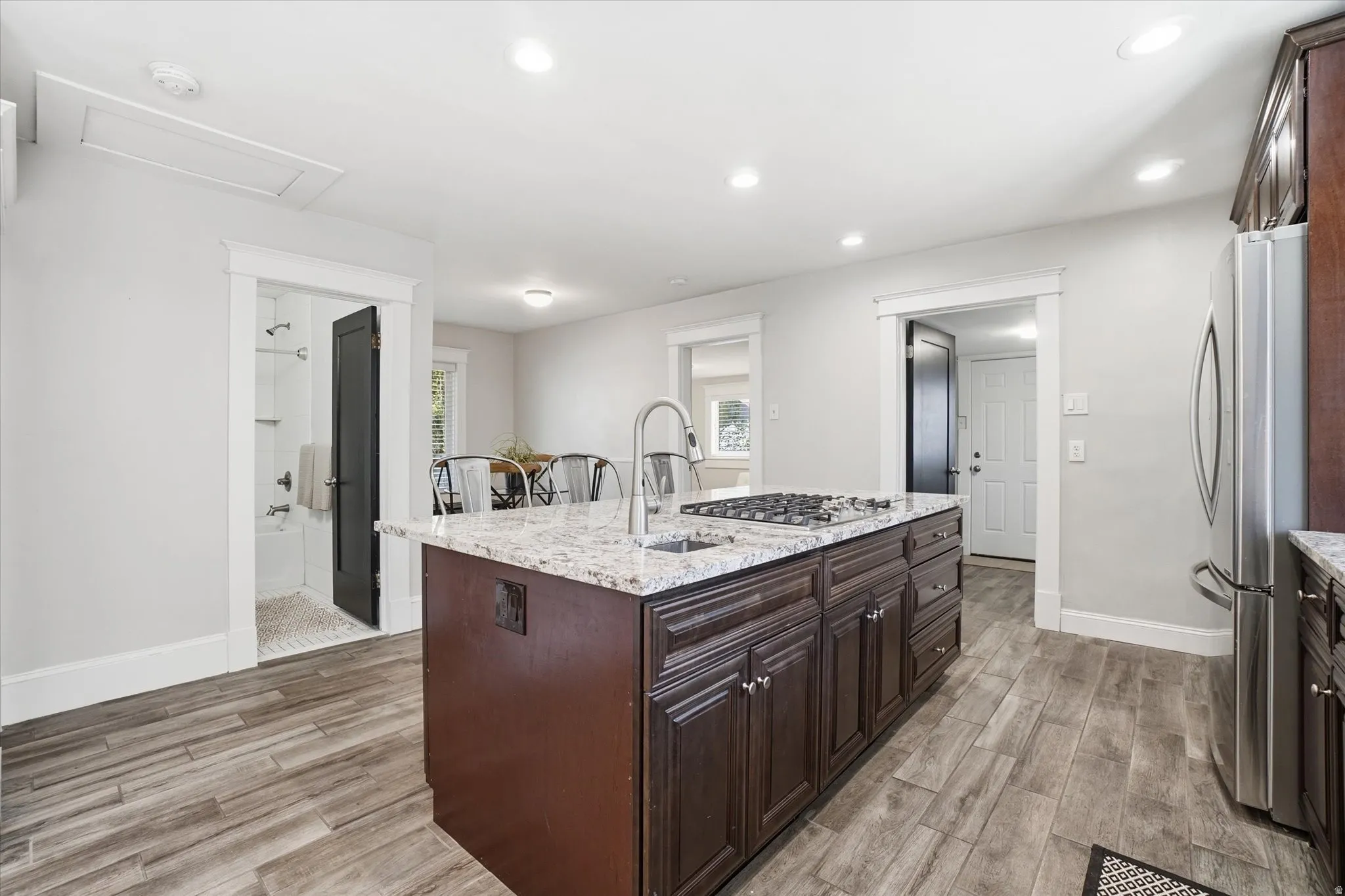 Kitchen island with dark wood cabinetry, integrated gas cooktop, and a stainless steel sink with a gooseneck faucet