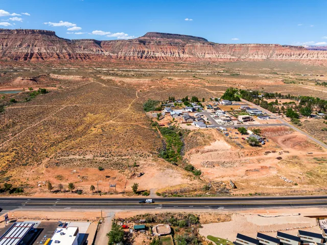Aerial perspective showcasing expansive red rock formations, a residential community with multiple single-family homes, and a prominent highway
