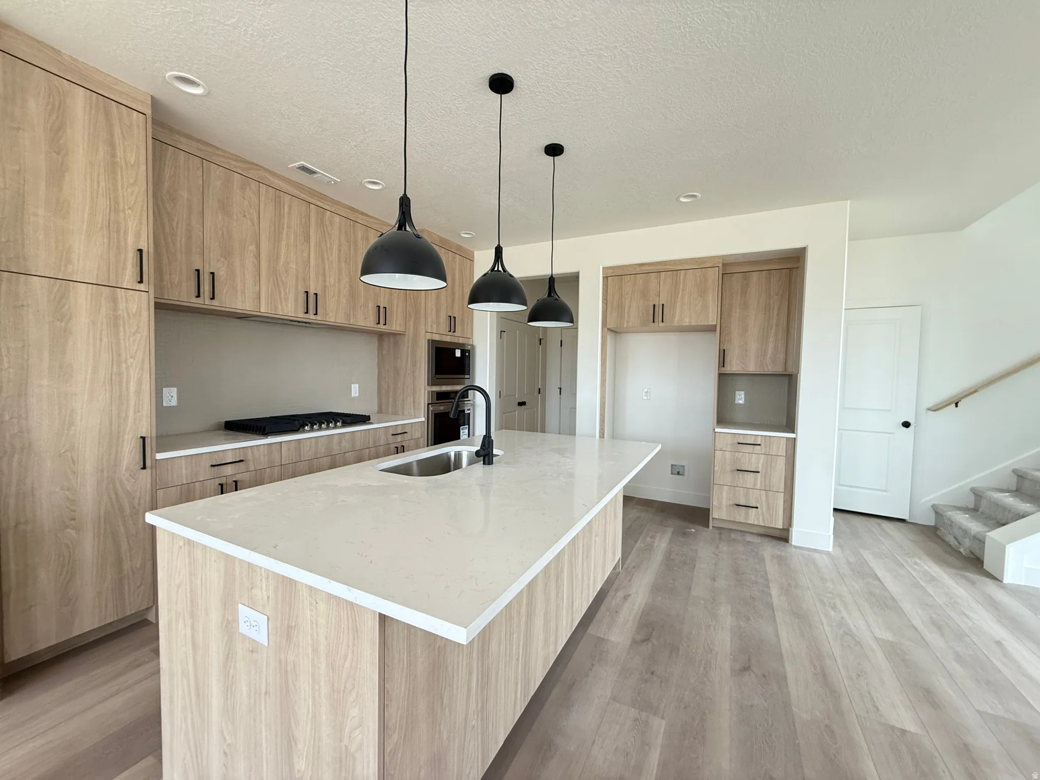 Contemporary kitchen featuring wood-finish cabinetry, light-toned countertops, and a large island with an undermount sink