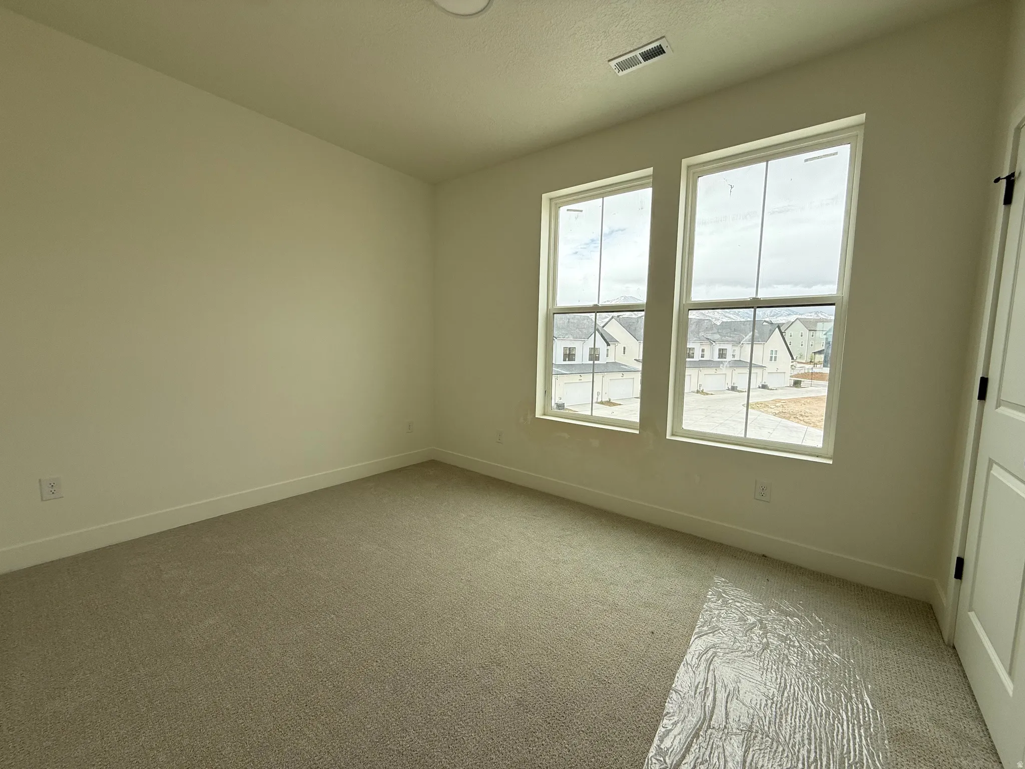 Neutral-toned room featuring a light beige carpet, white baseboards, and two tall windows