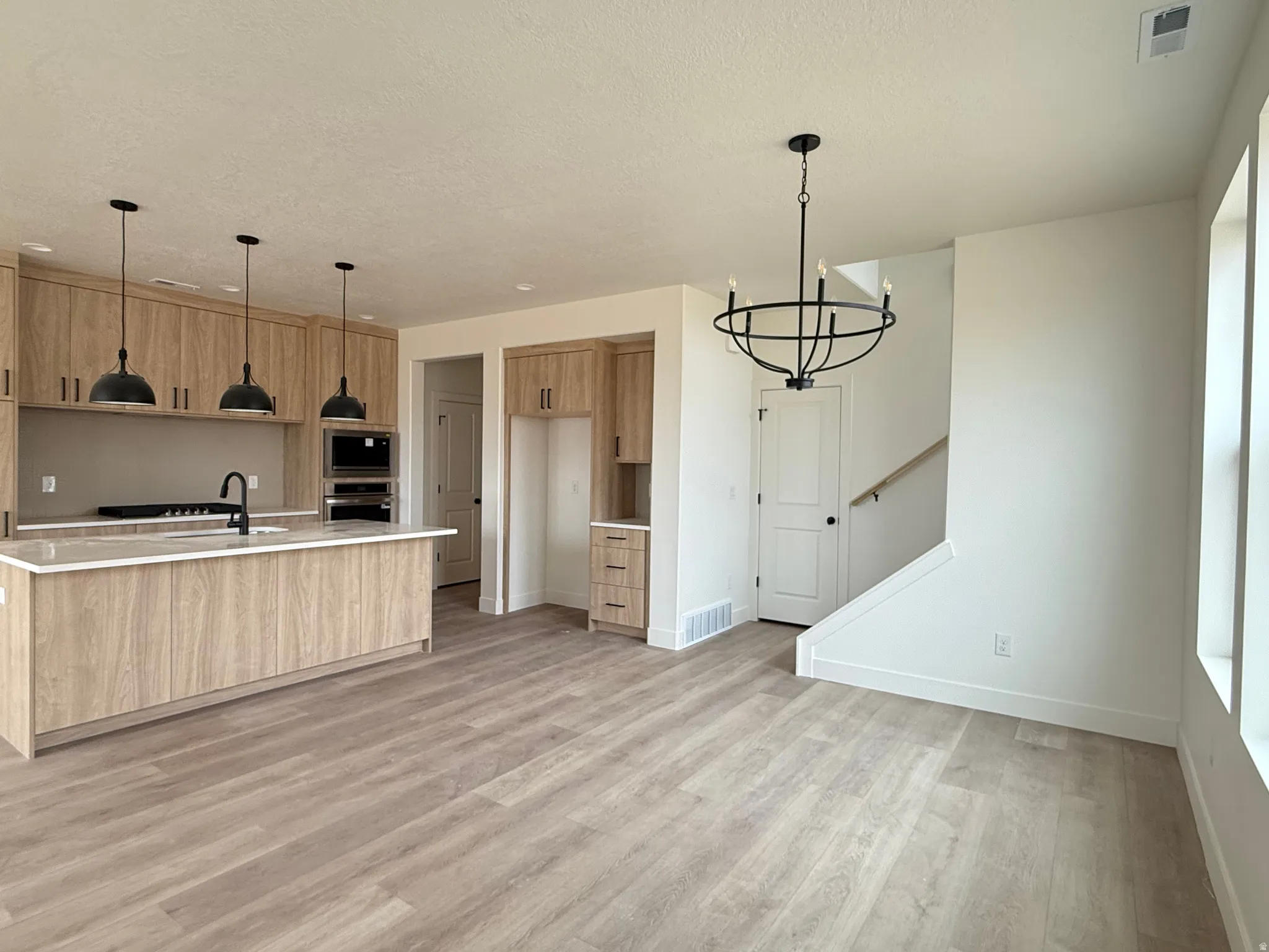 Open-concept kitchen and living area featuring wood-finish flooring, light-toned cabinetry, a central kitchen island with countertop, and integrated double ovens