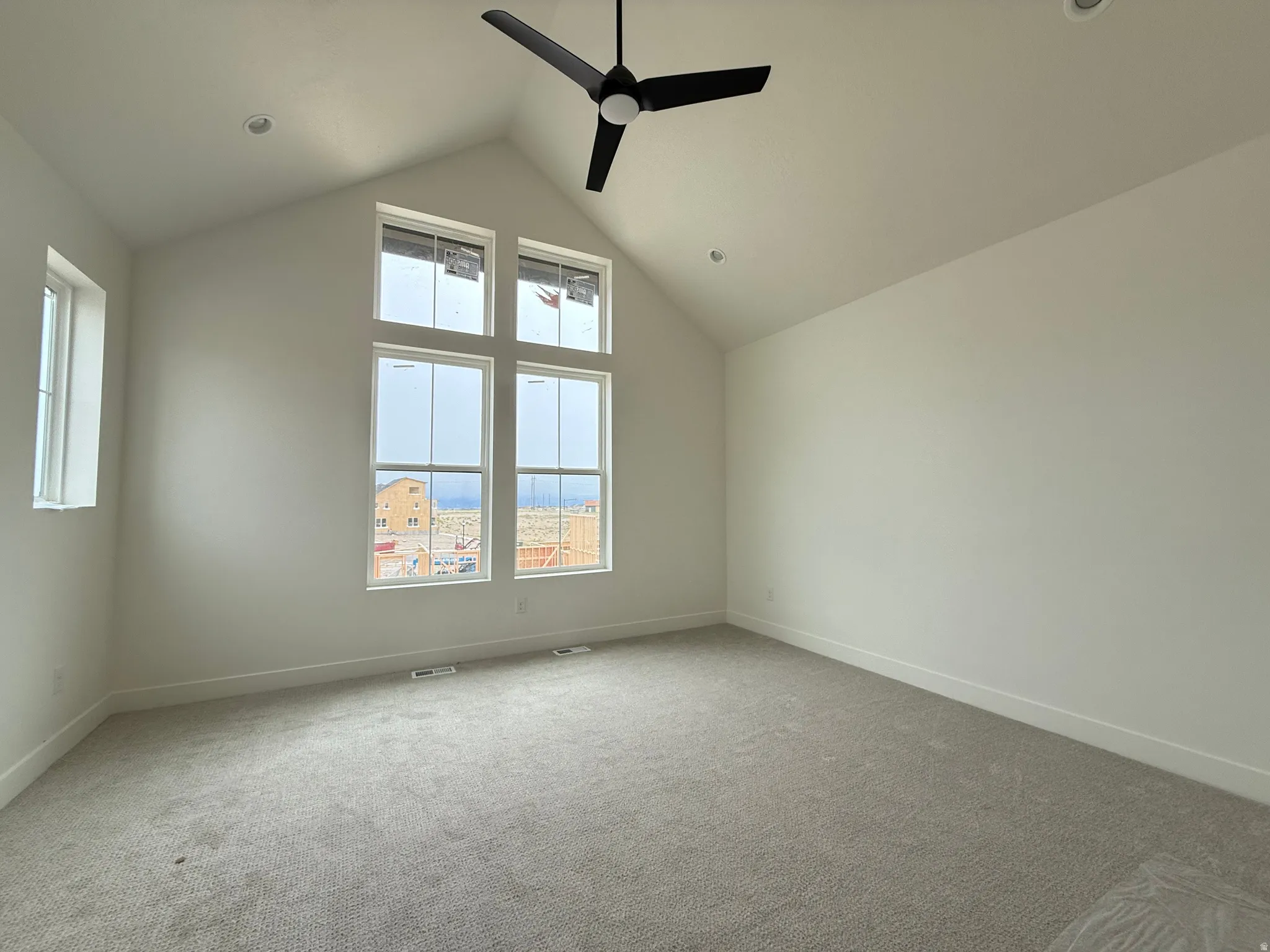 Vaulted ceiling room featuring a contemporary ceiling fan, recessed lighting, expansive windows, crisp white walls, and neutral carpeting