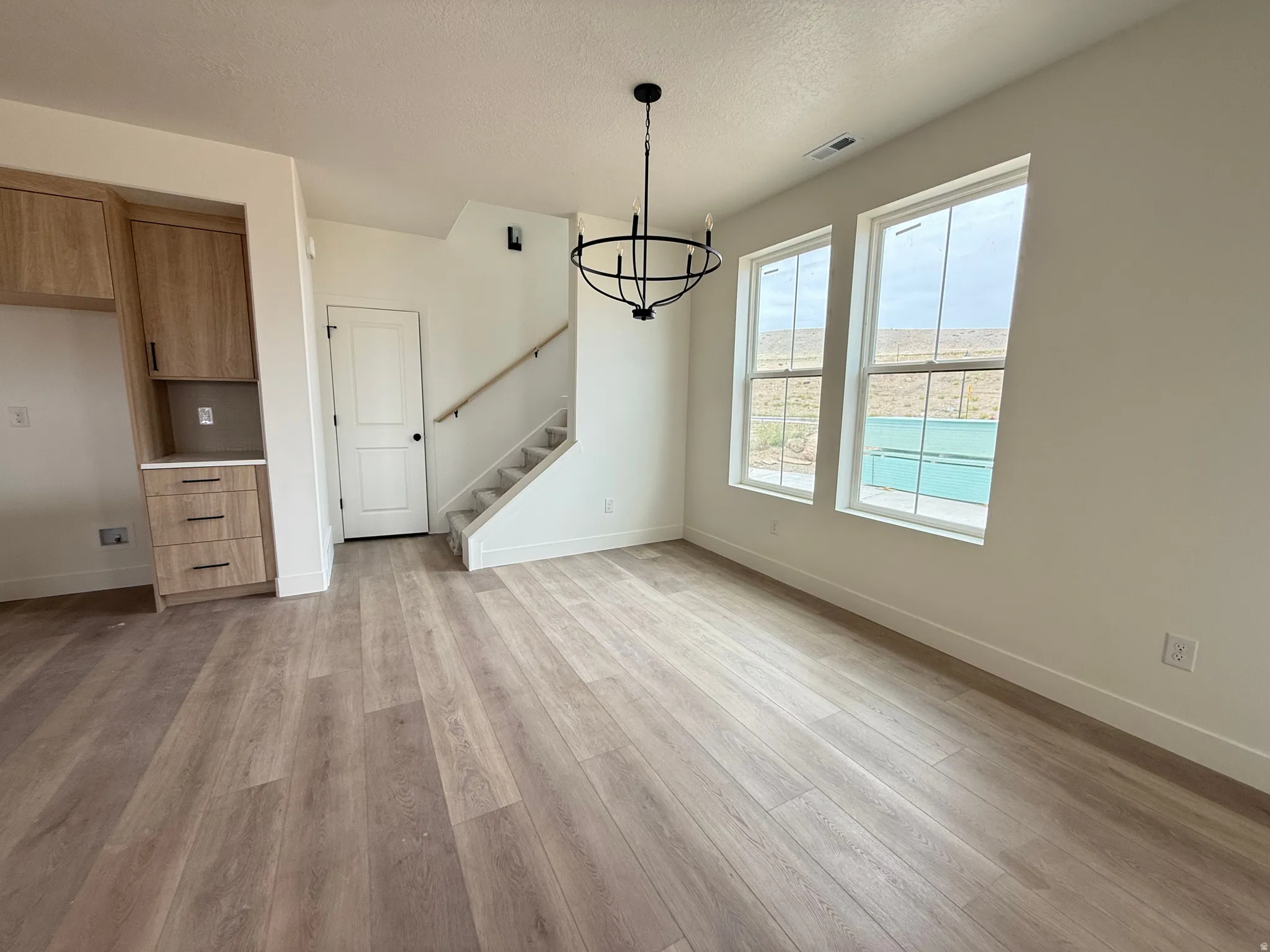 Open-concept living area featuring wood-finish flooring, built-in cabinetry with a light wood finish, and a contemporary black chandelier