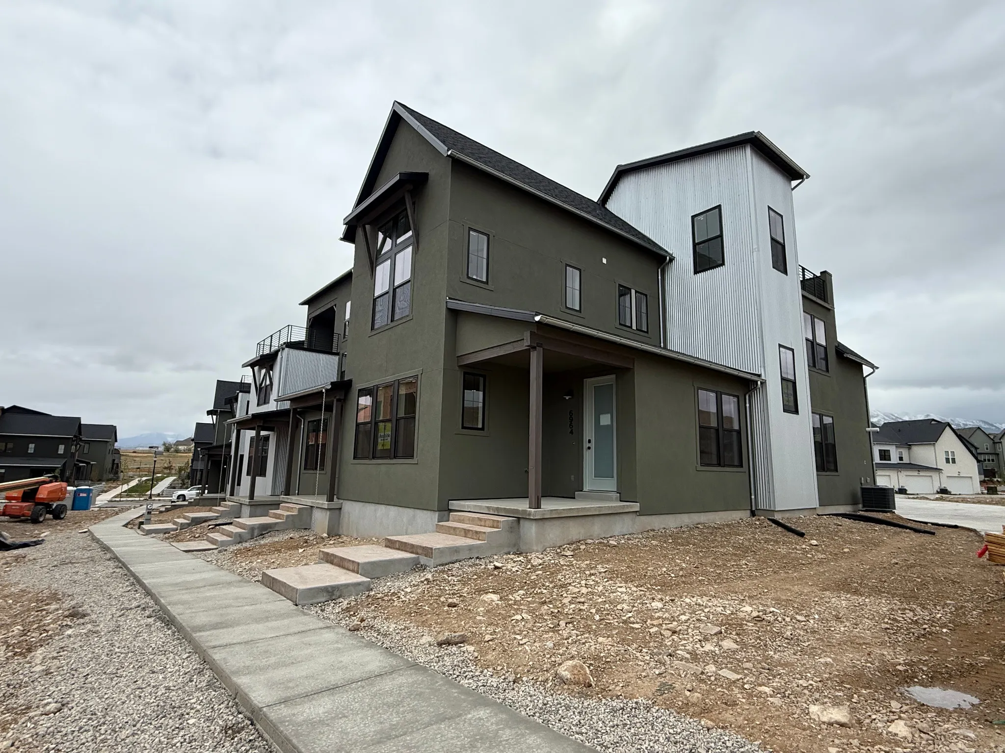Modern multi-level residence featuring a dark green stucco exterior with corrugated metal accents, black-framed windows, and a covered entry porch