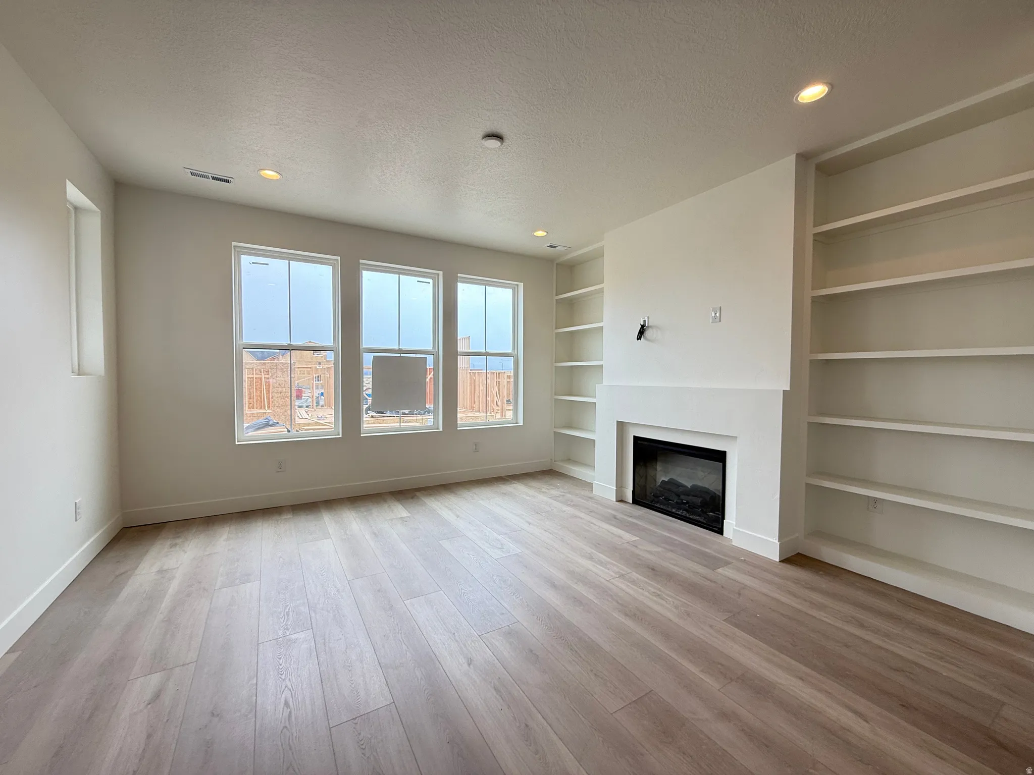 Spacious room featuring wood-finish flooring, a built-in fireplace with a mantel, integrated shelving, recessed lighting, and multiple windows