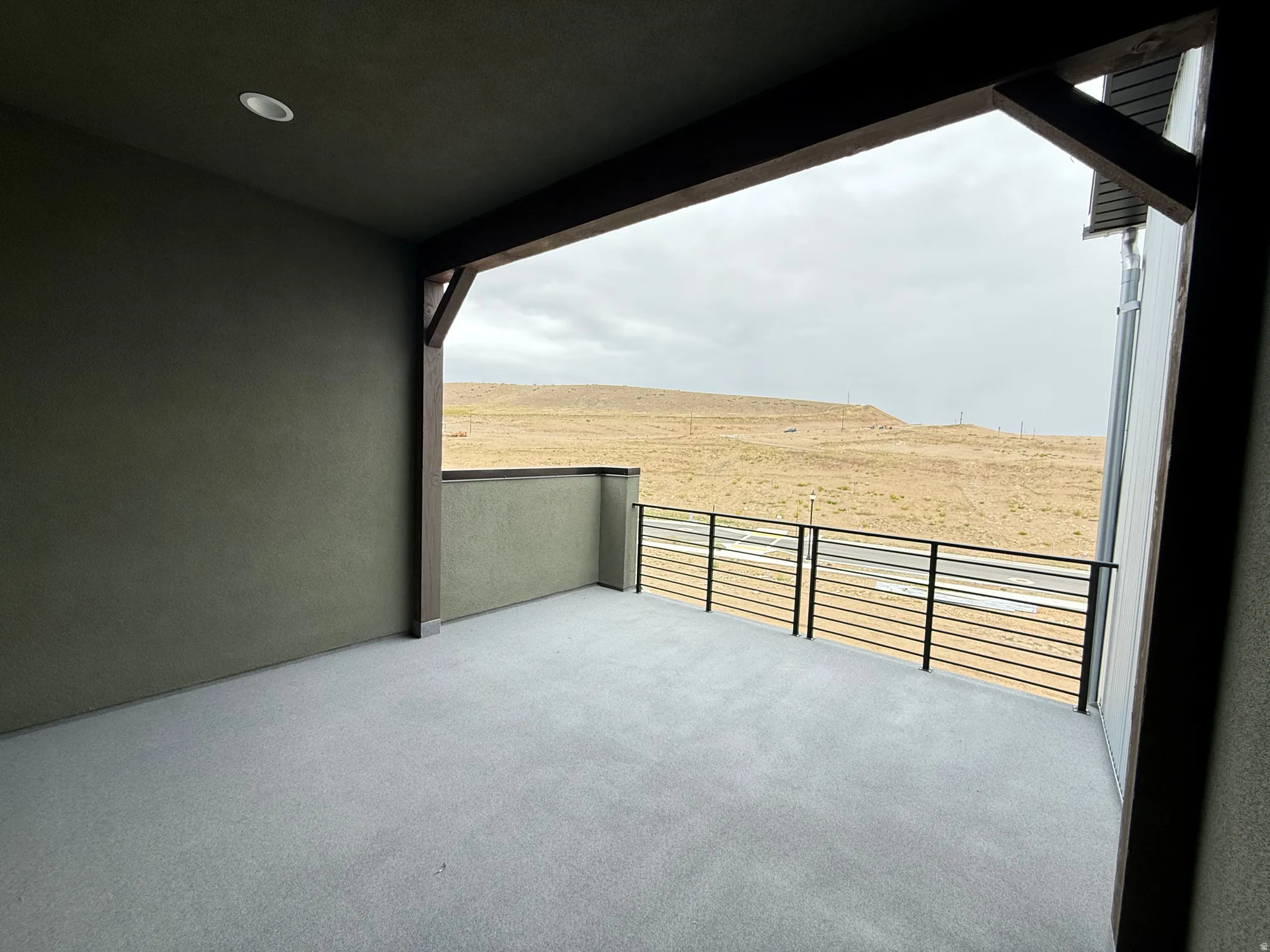 Spacious covered balcony featuring recessed lighting, a modern horizontal bar railing, and a durable concrete floor, complemented by stucco exterior walls