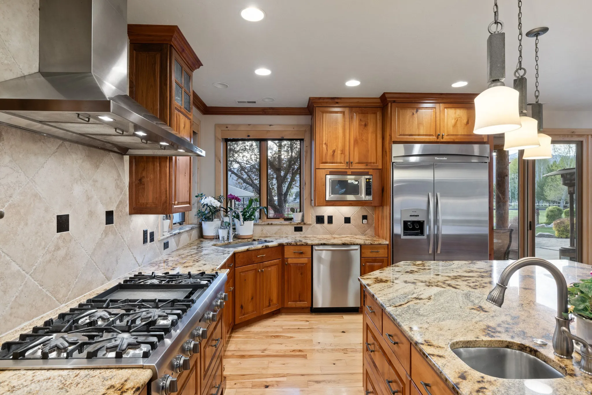 Kitchen featuring wood finish cabinets, built in appliances, light wood finished floors, light stone countertops, and ornamental molding