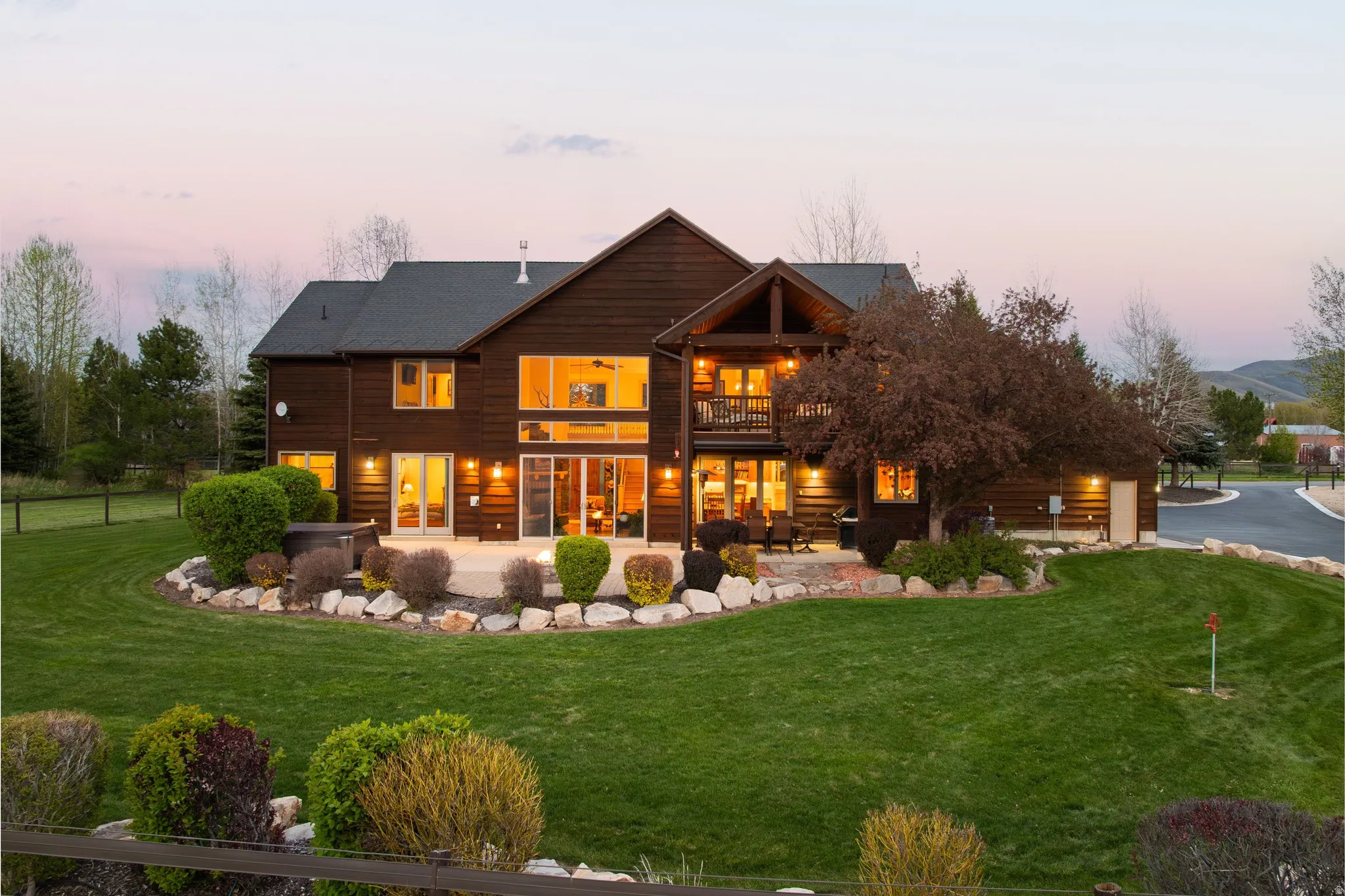 Back of house at dusk featuring a balcony, a lawn, and a patio