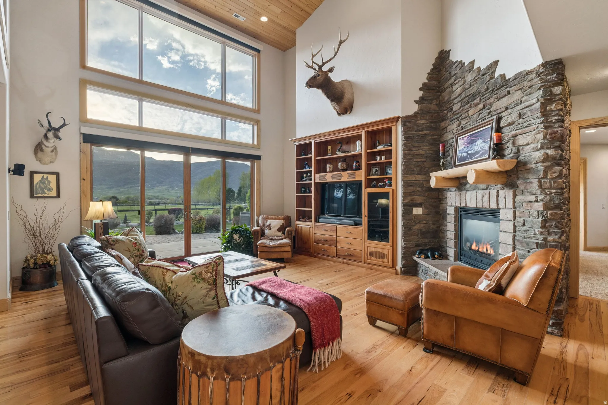 Living room with a stone fireplace, light wood-style floors, healthy amount of natural light, recessed lighting, and a high wood ceiling