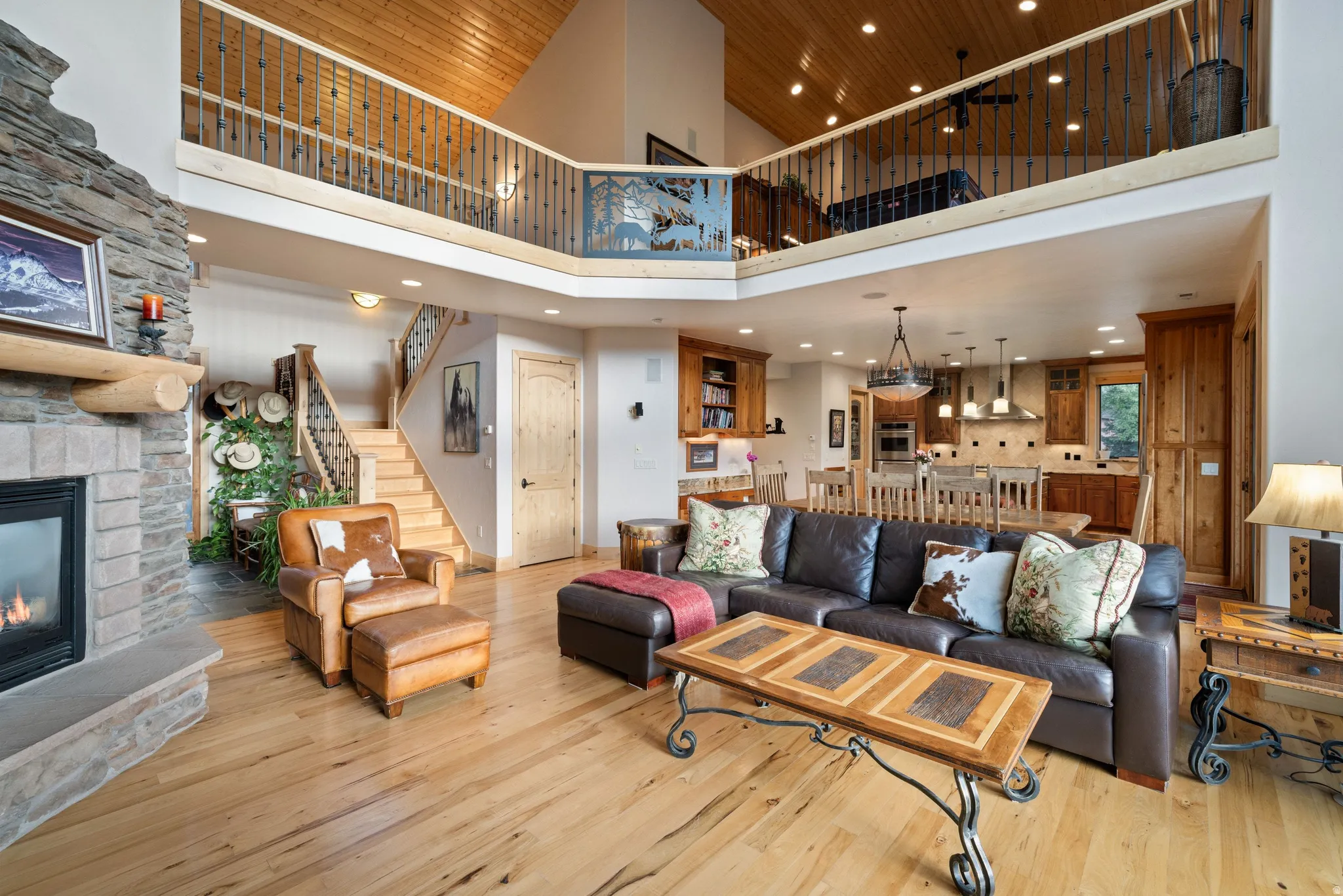 Living room with a stone fireplace, light wood finished floors, a high wood ceiling, and hanging lights