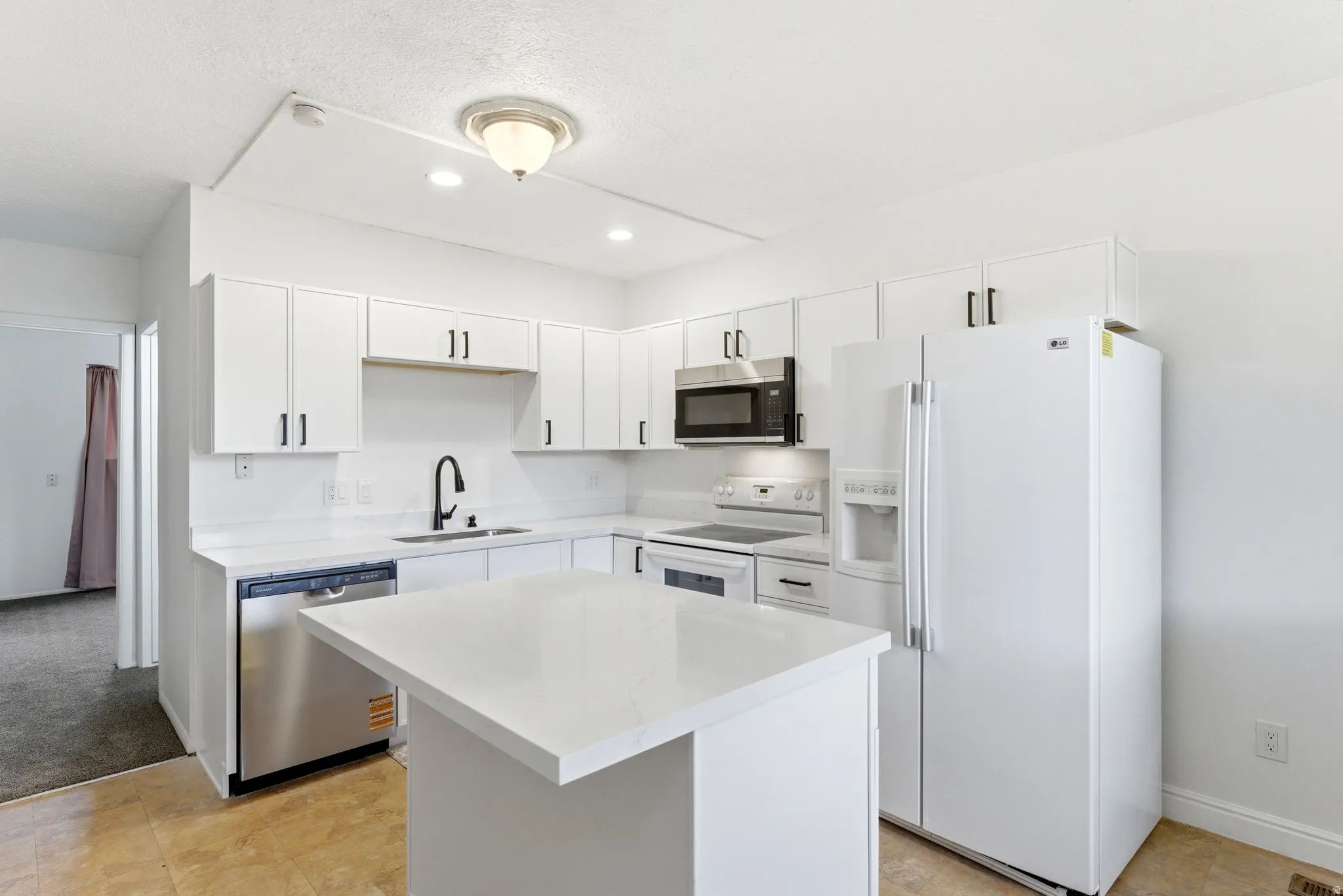 Bright kitchen featuring white cabinetry with dark pulls, white countertops, stainless steel dishwasher, and a center island