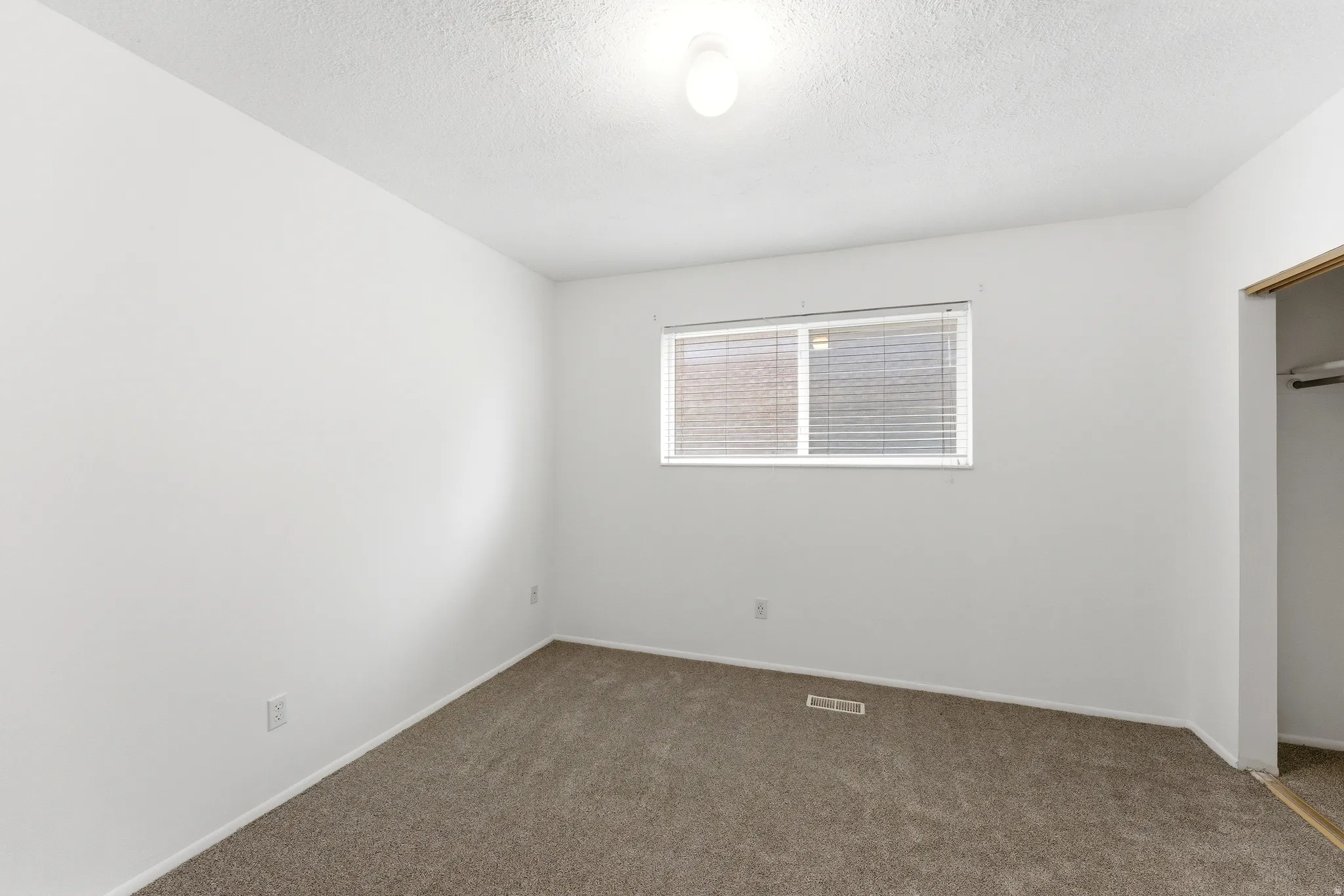 Room featuring neutral-toned carpeting, white walls, and a single window with blinds