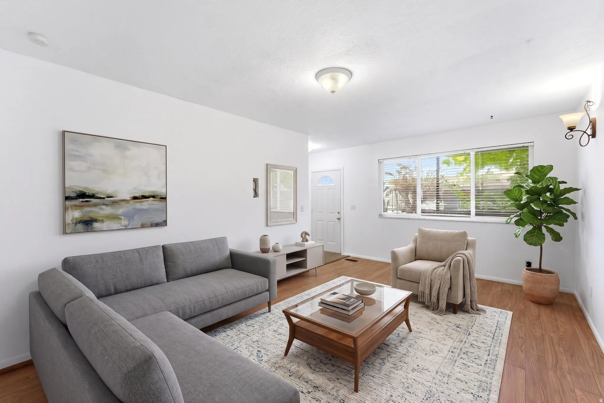 Open concept living area featuring wood-finish flooring, white walls, and a large window with horizontal blinds