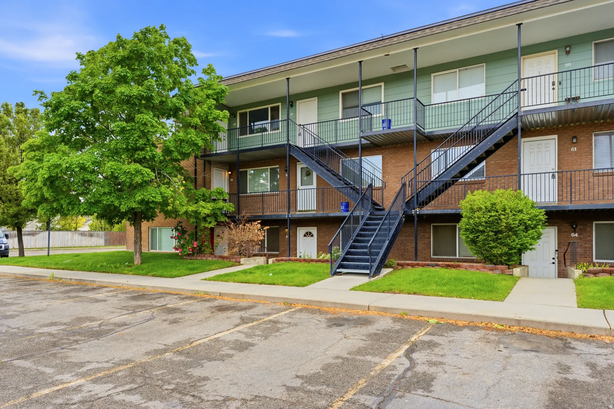 Multi-story apartment building featuring brick and siding exterior, black metal exterior staircases, individual balconies with black railings, and a concrete parking area