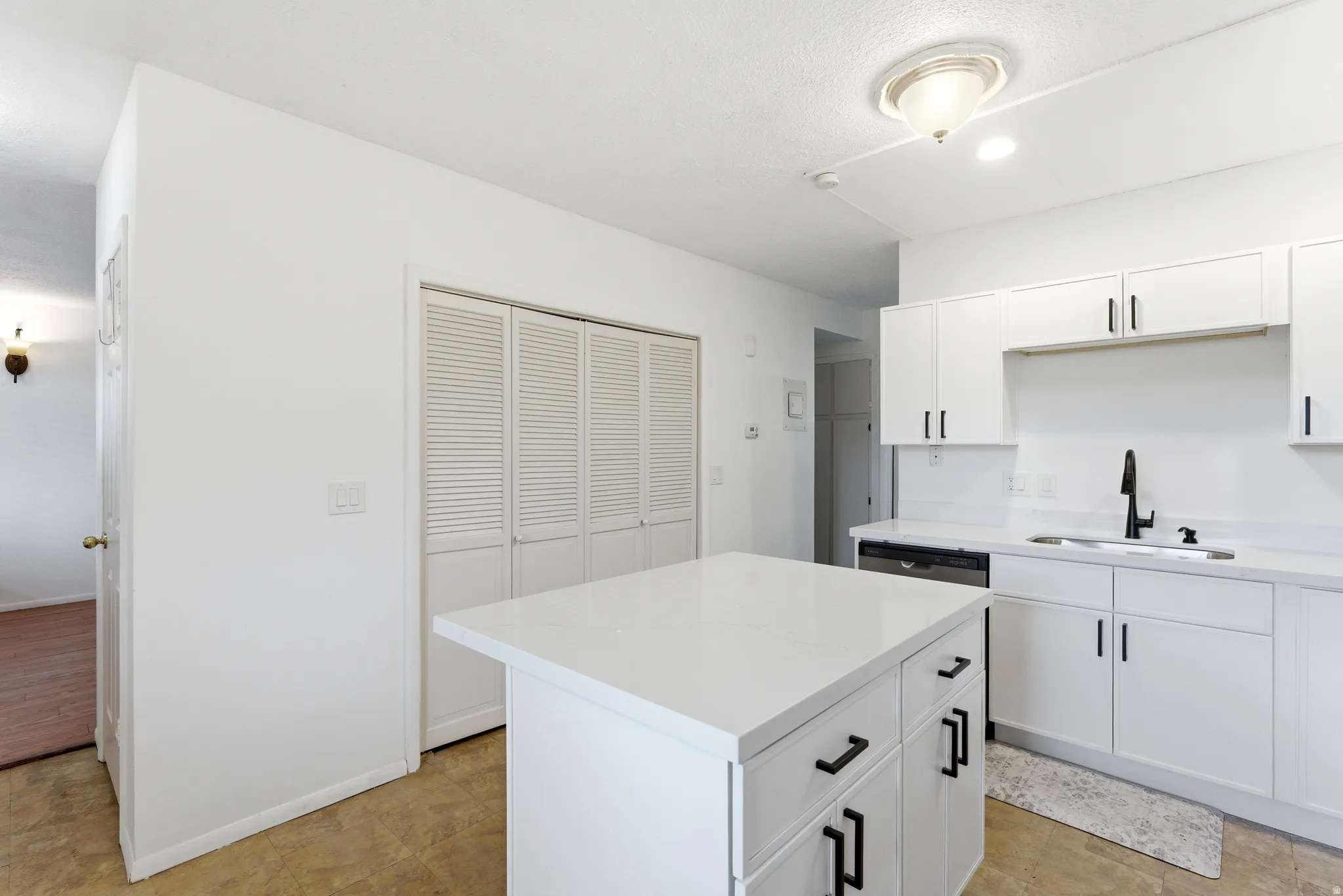 Modern kitchen featuring a central island with white countertop, white cabinetry with black hardware, a stainless steel dishwasher, and a black faucet
