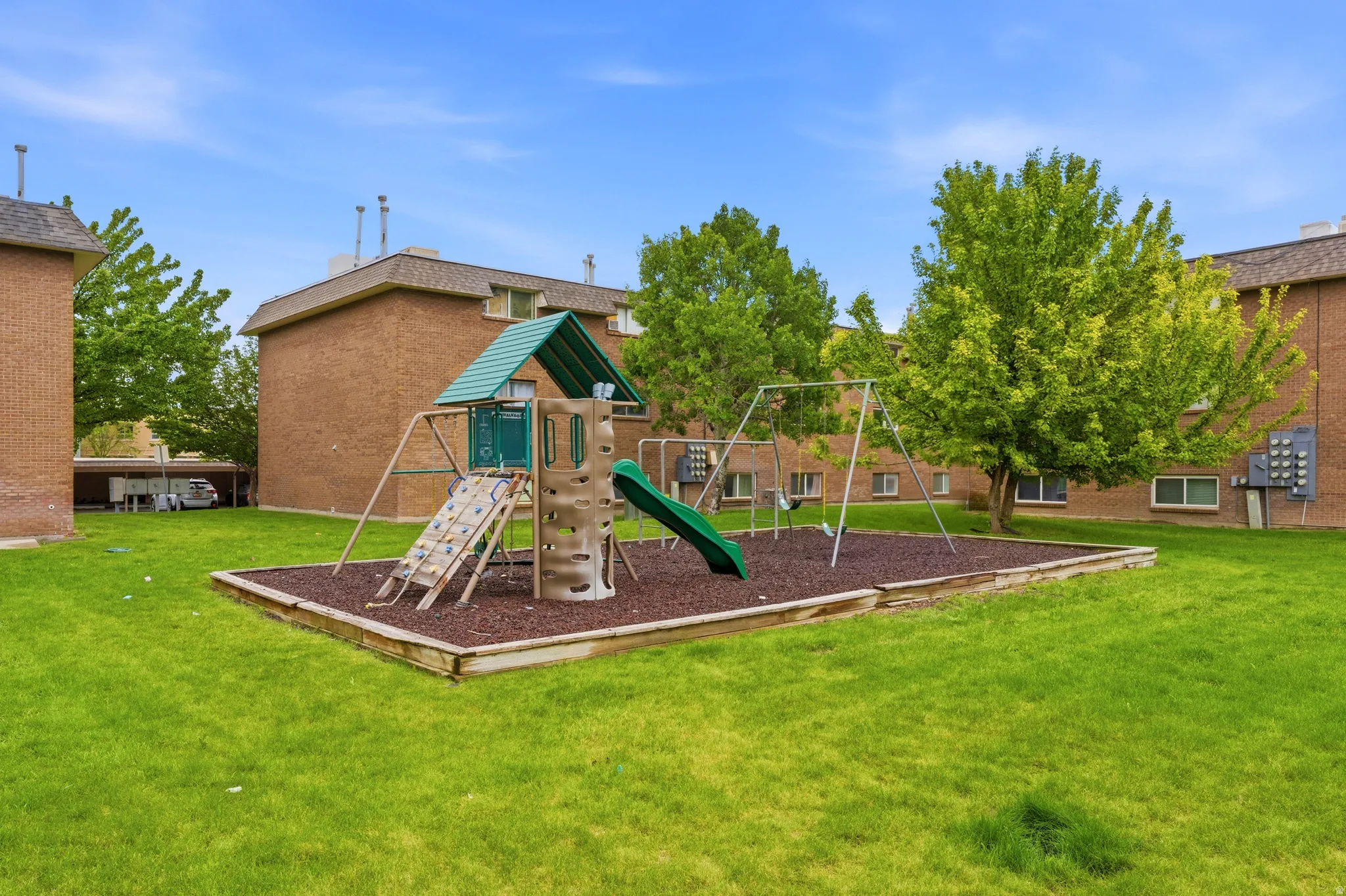 Outdoor recreational area featuring a multi-level play structure with slide, climbing wall, and swings