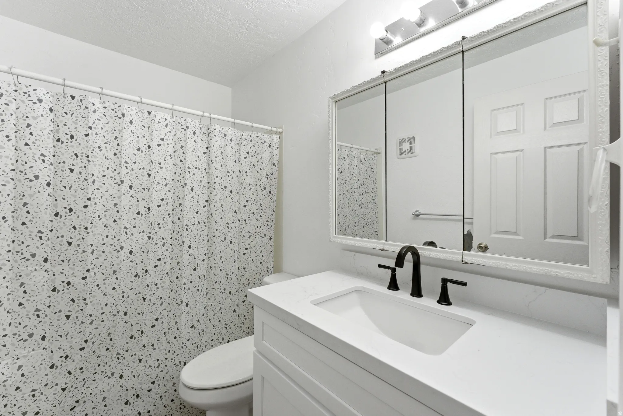 Bathroom featuring a white vanity with an integrated sink, matte black faucet, and a wall-mounted mirrored medicine cabinet with integrated lighting