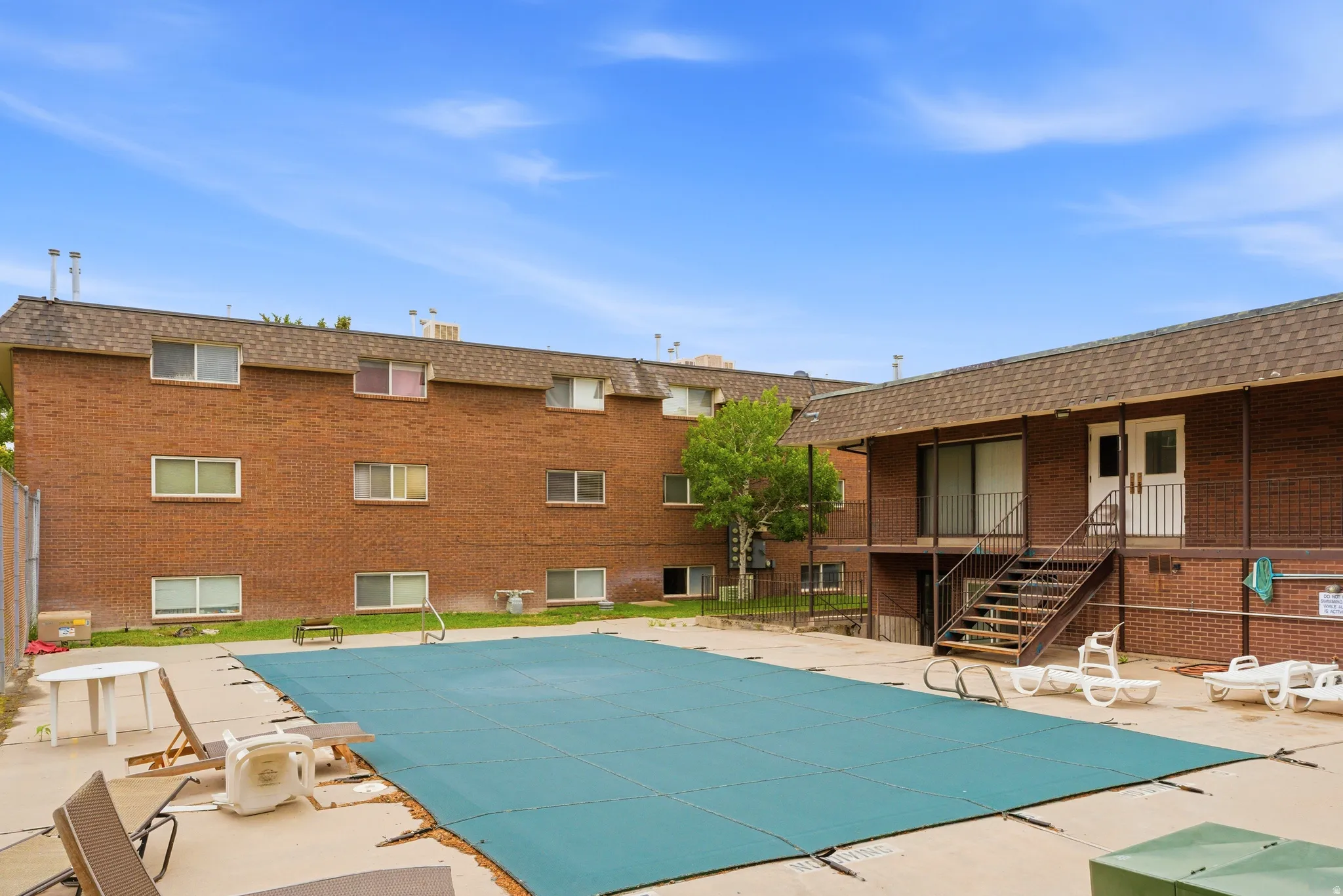 Outdoor swimming pool area with a covered pool, concrete surround, and brick building with multiple windows